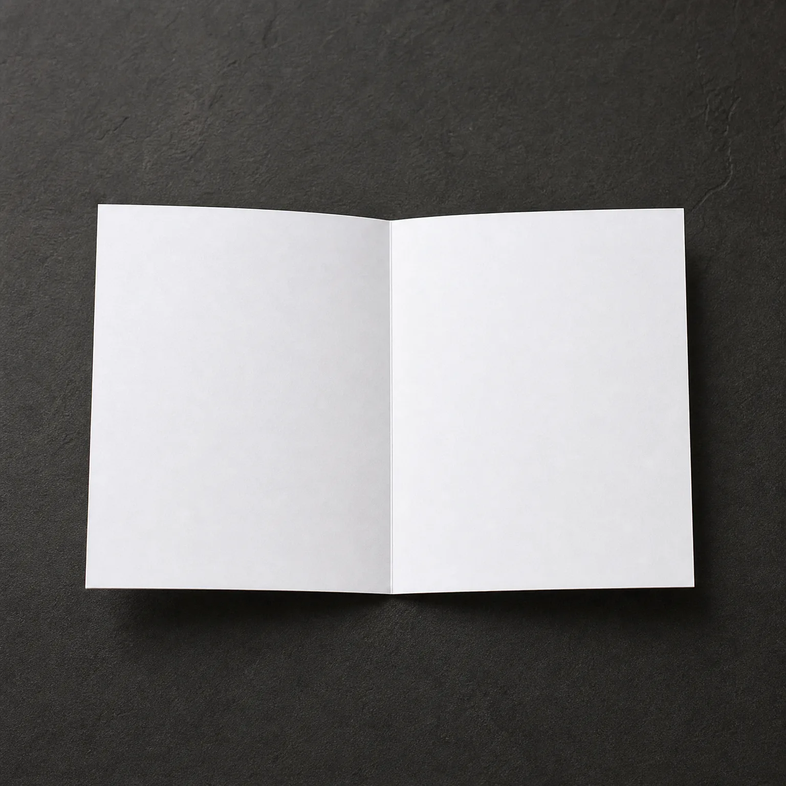 A blank white folded card standing open on a dark gray textured surface.