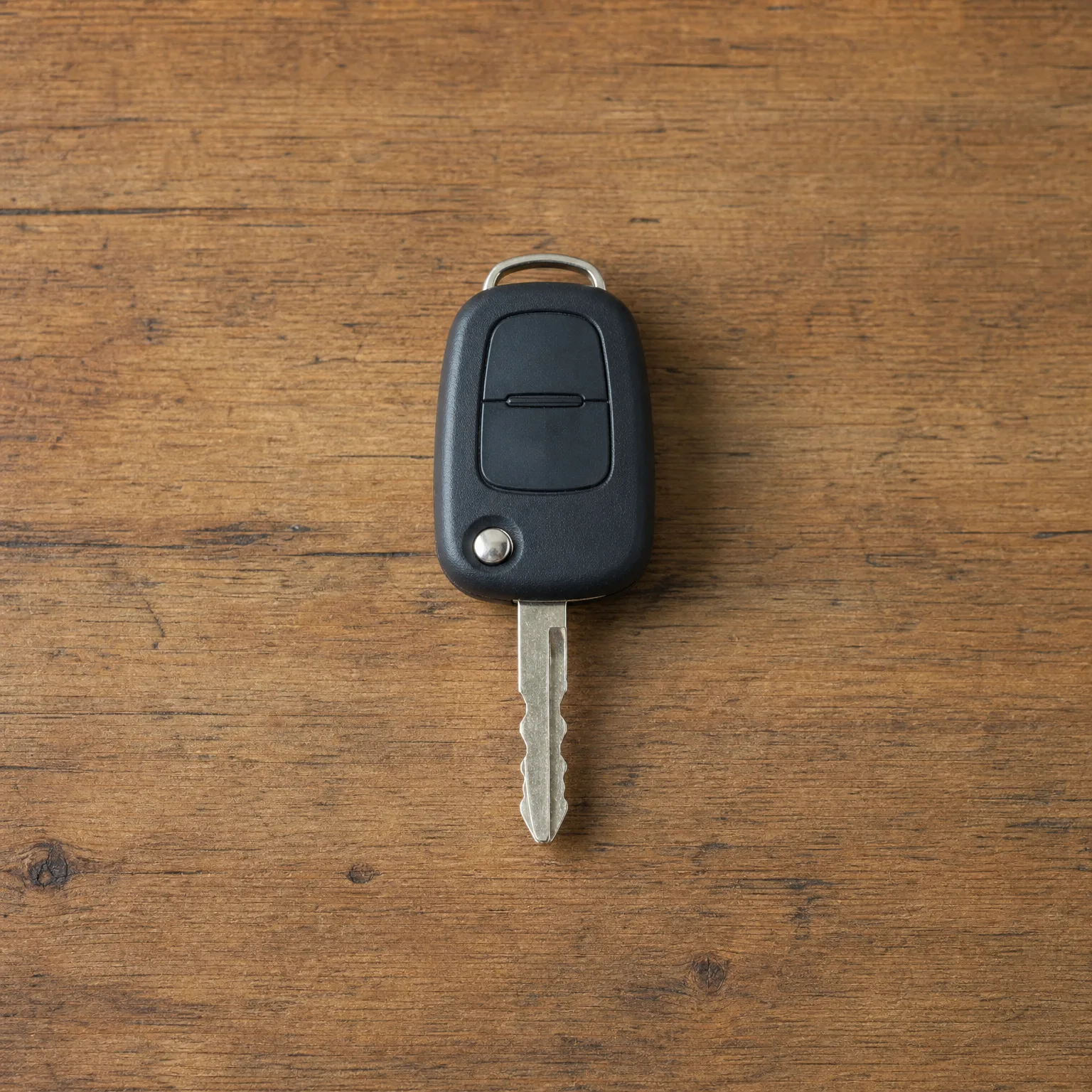 A black remote car key with a metal blade and key ring loop lying on a weathered brown wooden surface.