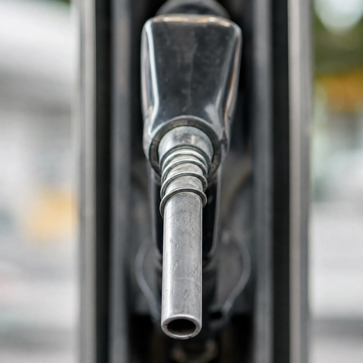 Close-up of a metal fuel nozzle on a pump, pointing toward the camera against a blurred background.