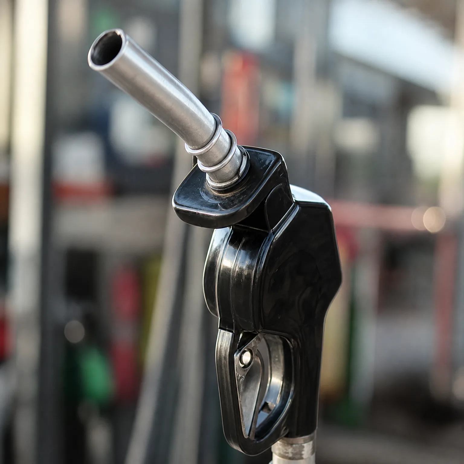 Close-up of a black fuel nozzle with a metal spout, photographed against a blurred background.