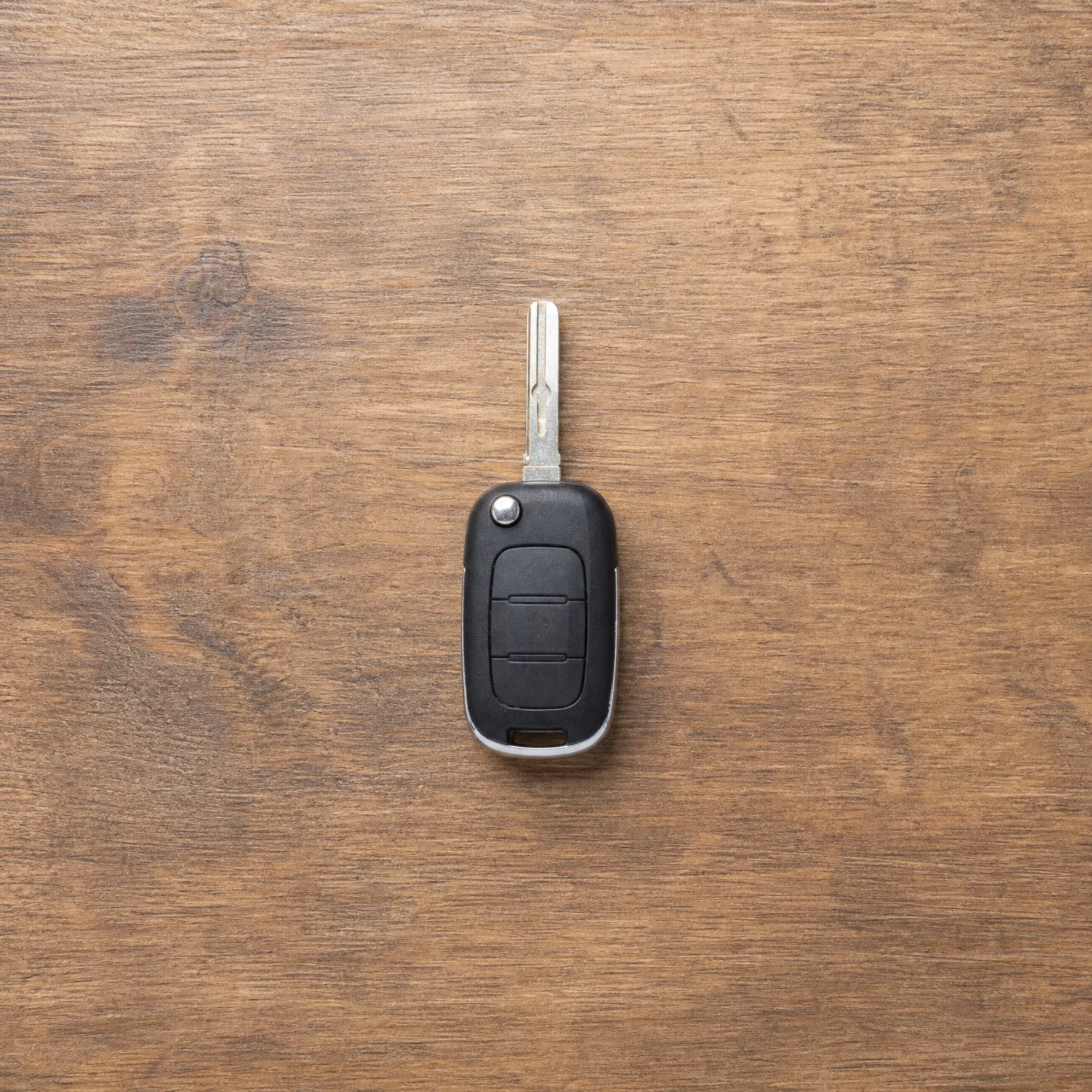 A black flip-style car key with two buttons and an exposed metal blade lying on a brown wood surface.