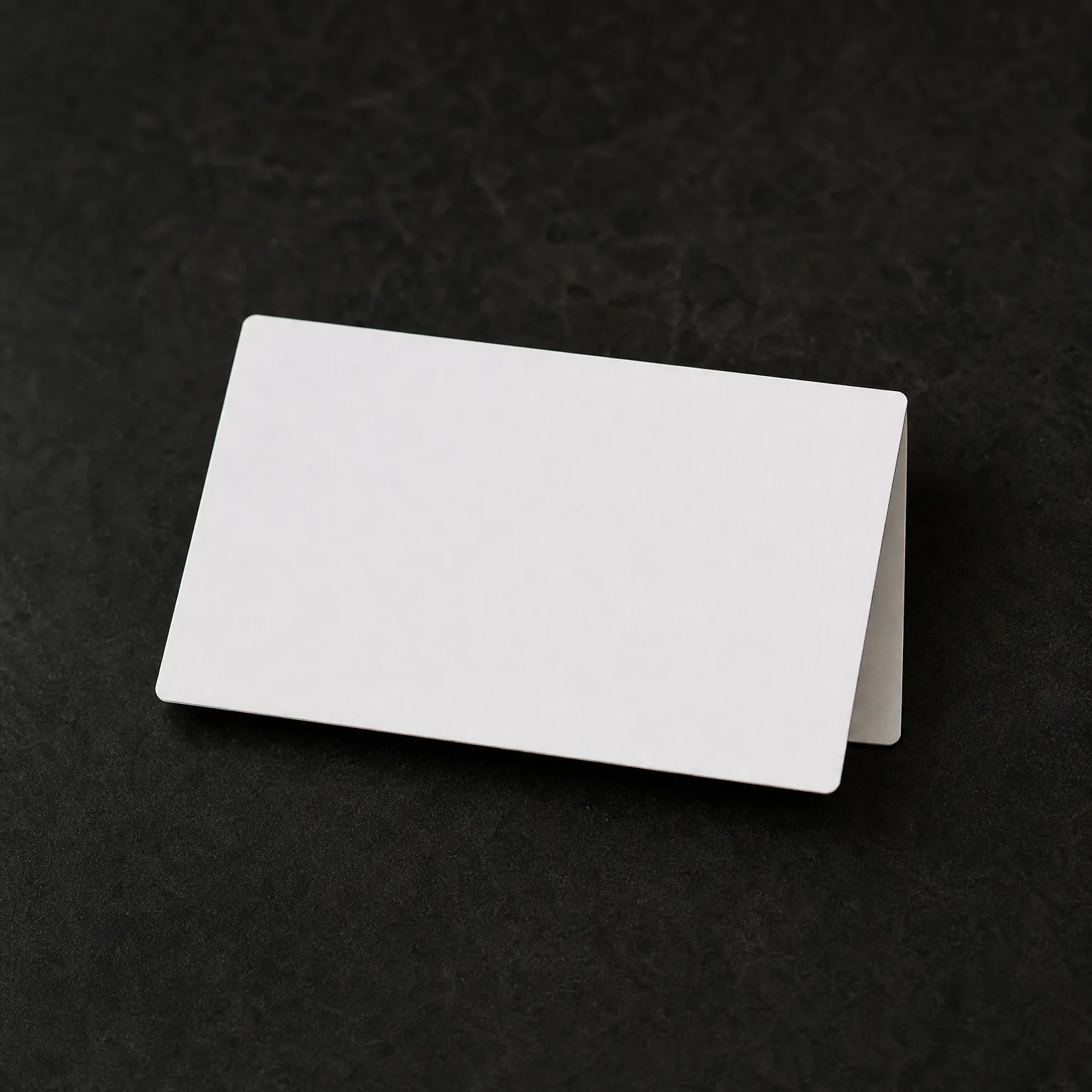 A blank white folded card standing tent-style on a dark textured surface.
