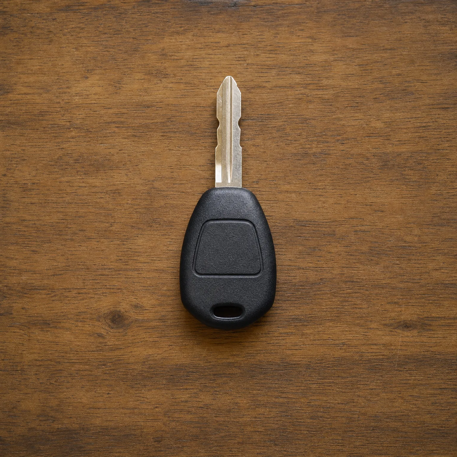 A car key with a black plastic head and cut metal blade lying on a brown wooden surface.