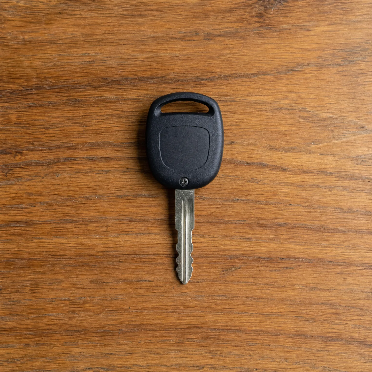 A single key with a black plastic head and cut metal blade lying on a wooden surface.