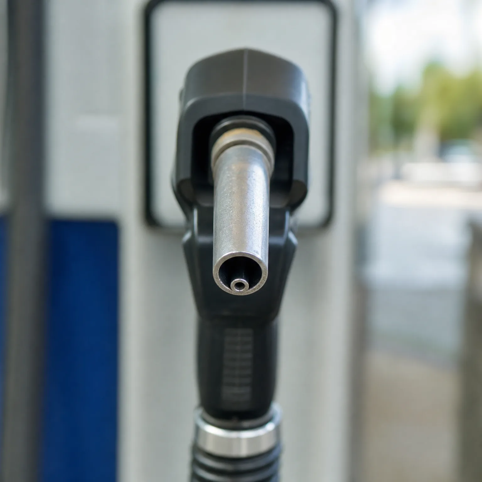 Close-up of a black fuel nozzle with a metal spout resting in a fuel pump holster, with a blurred background.