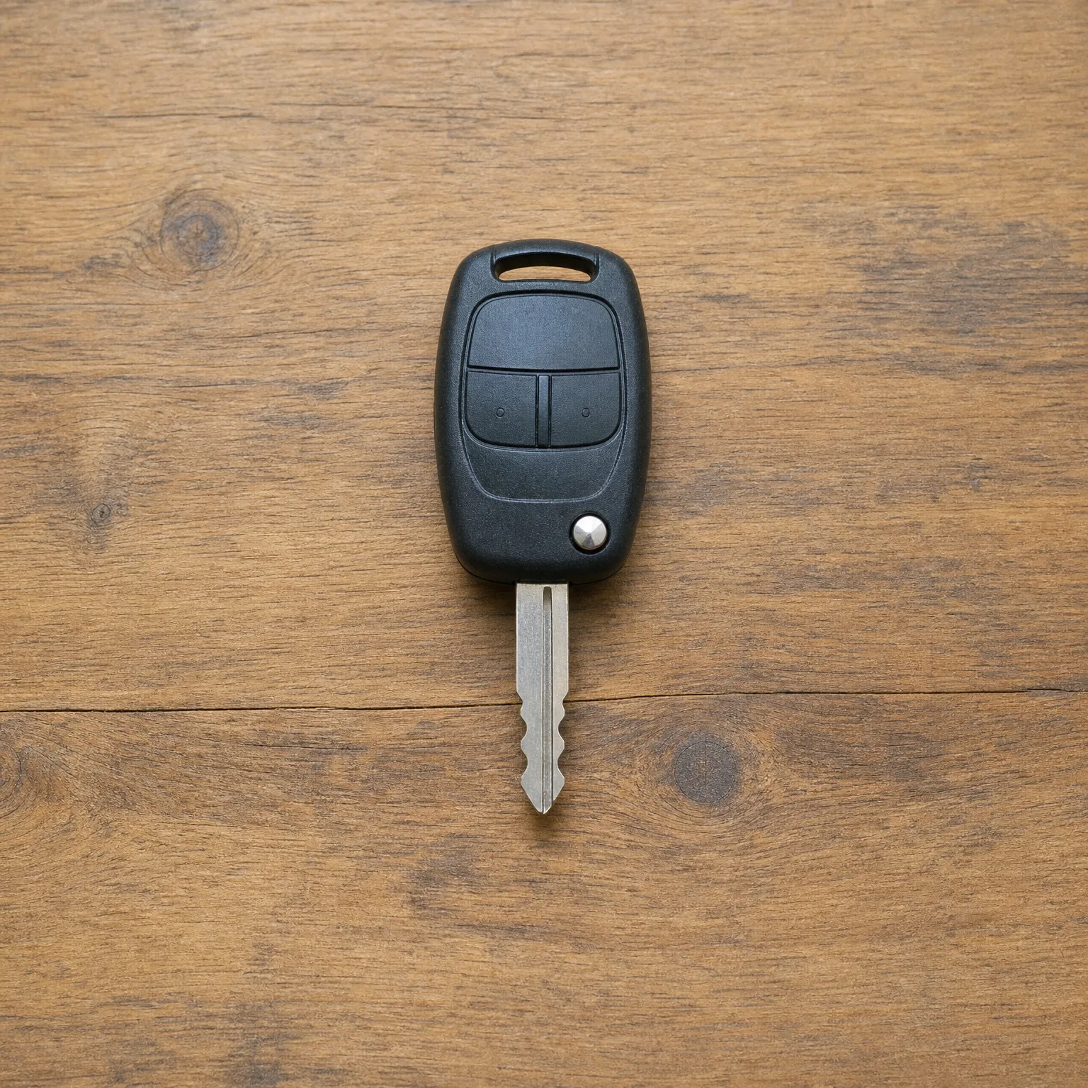 A black two-button remote car key with an exposed metal blade lying on a wooden surface.