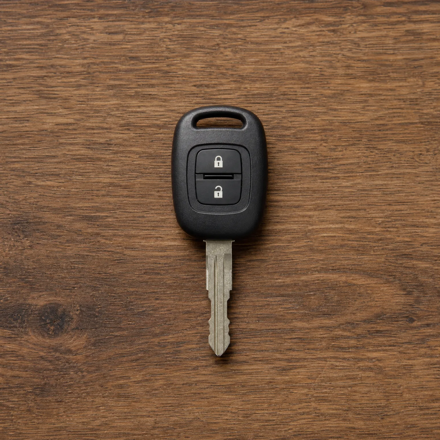 A black two-button remote car key with an uncut-style metal blade lying on a dark wood-grain surface, photographed from above.