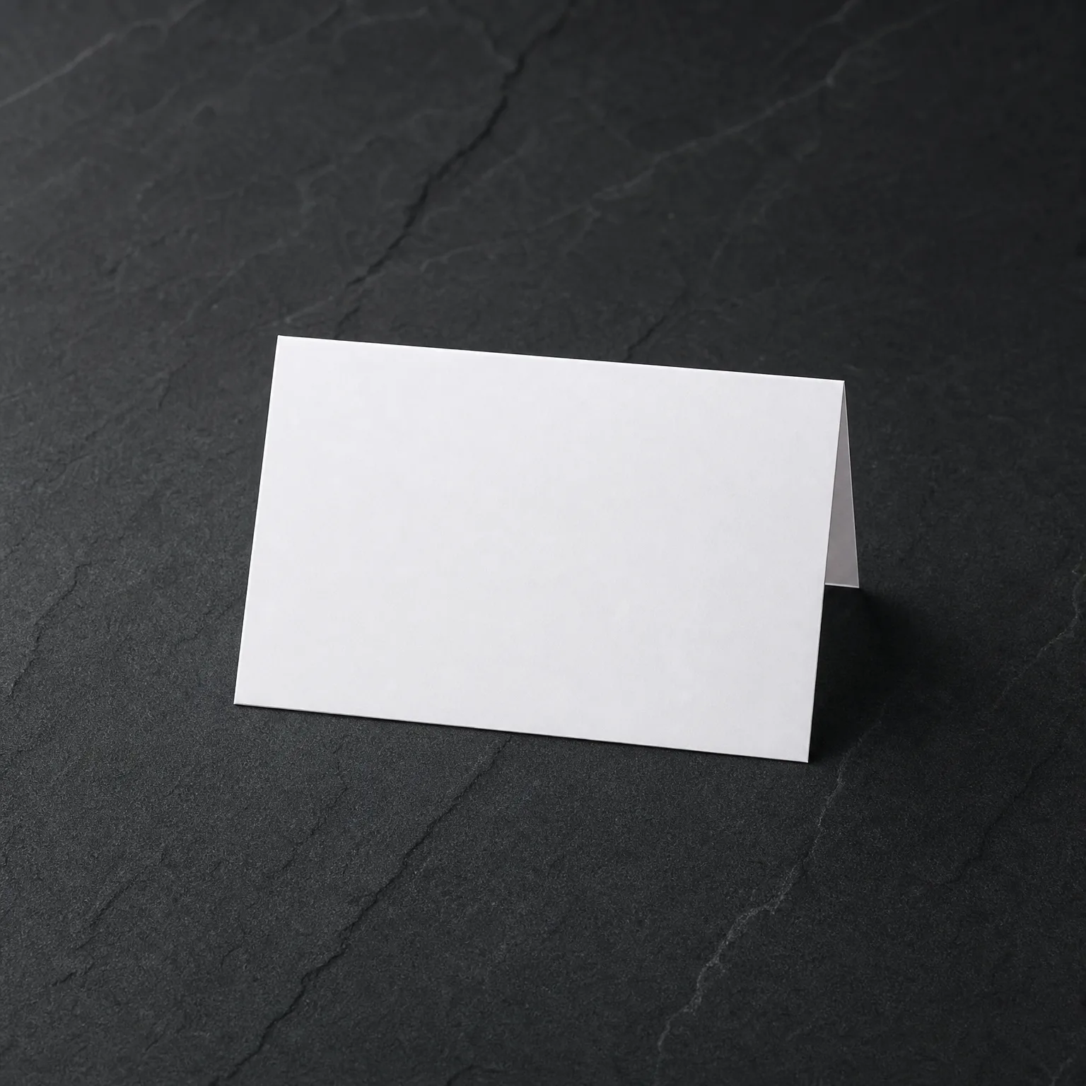 A blank white folded tent card standing on a dark gray textured stone surface.
