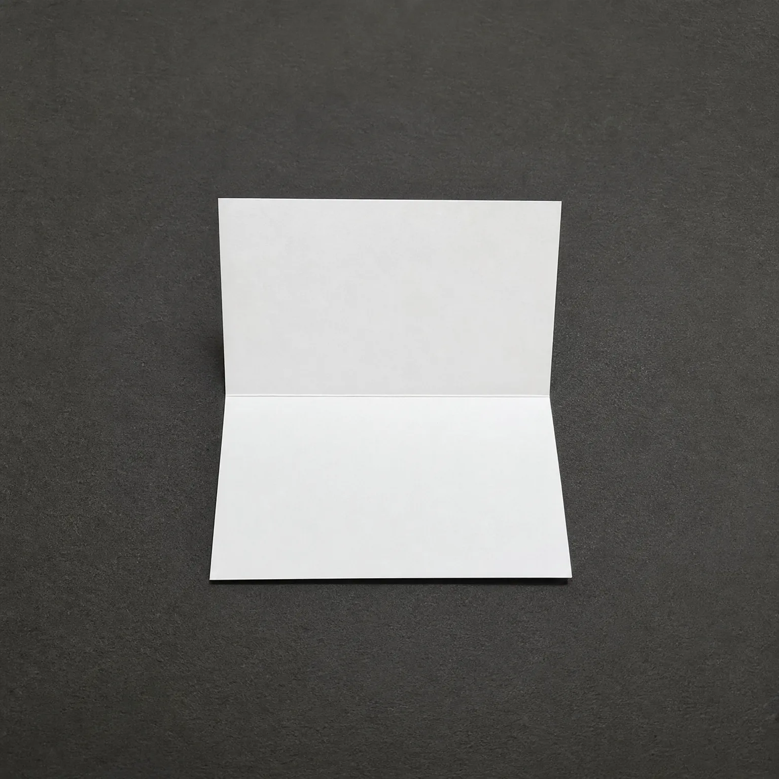 A blank white folded card standing open on a dark gray textured surface.
