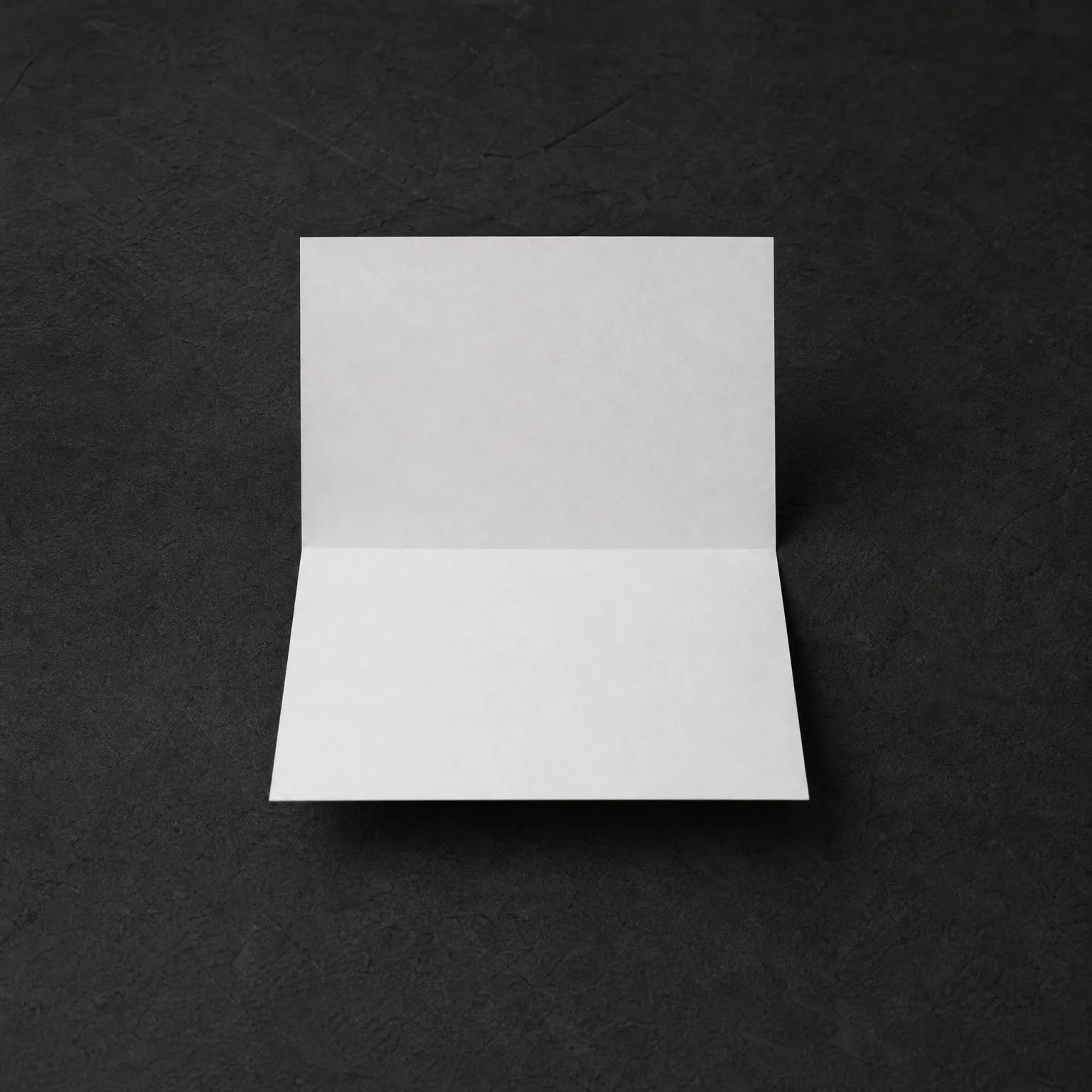 A blank white folded card standing open on a dark textured gray surface.