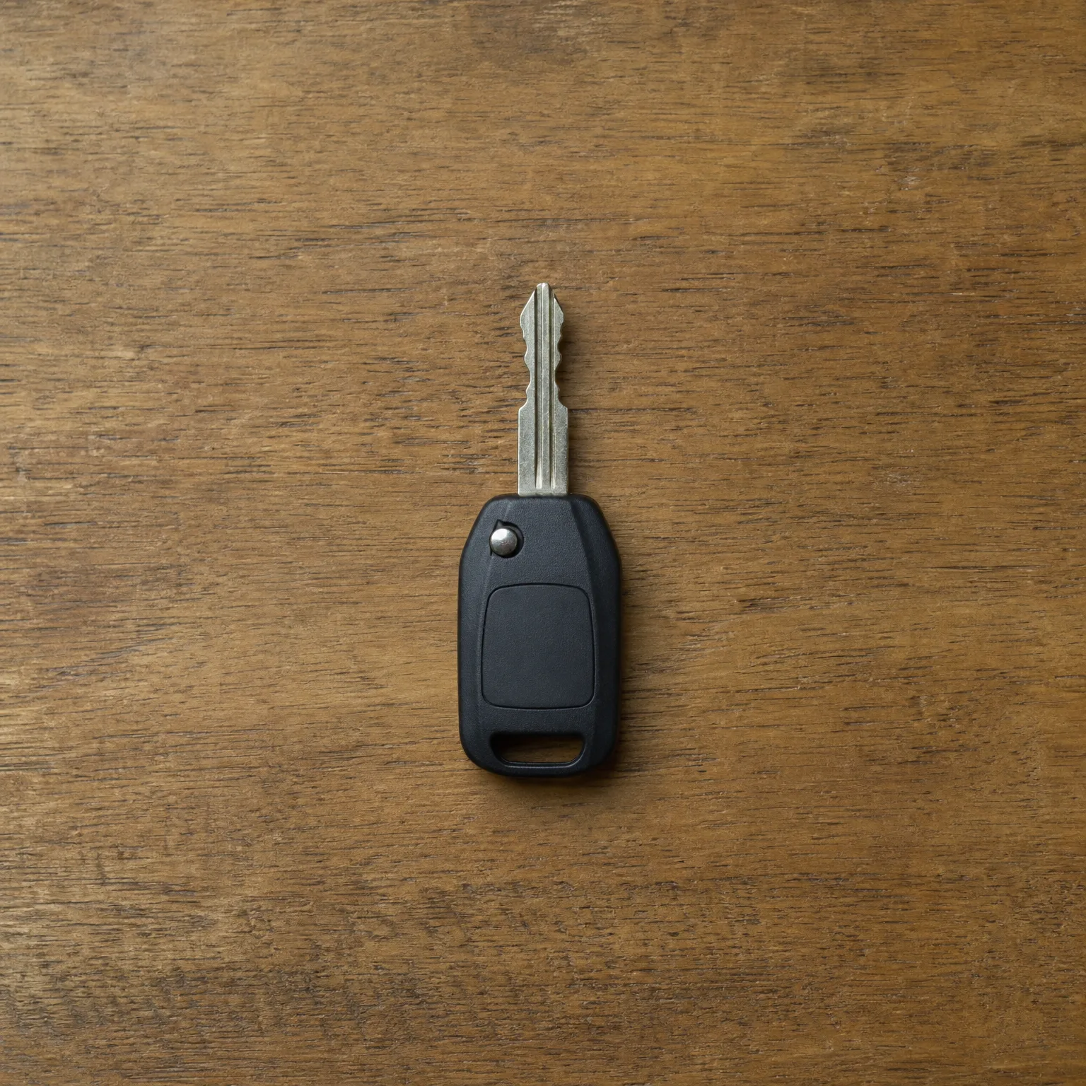 A black plastic-headed car key with a cut metal blade lying on a wooden surface.