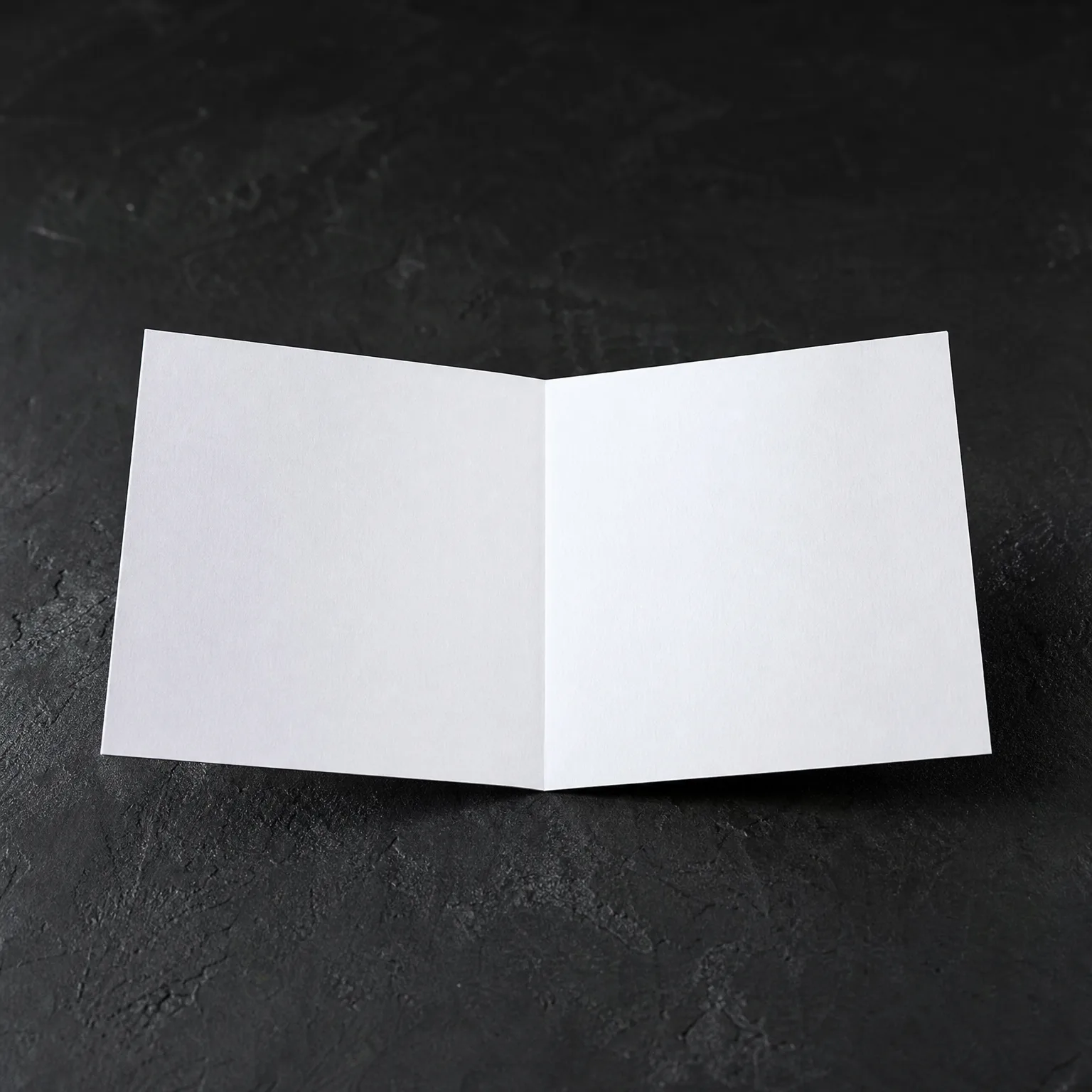 A blank white folded card standing open on a dark textured surface.