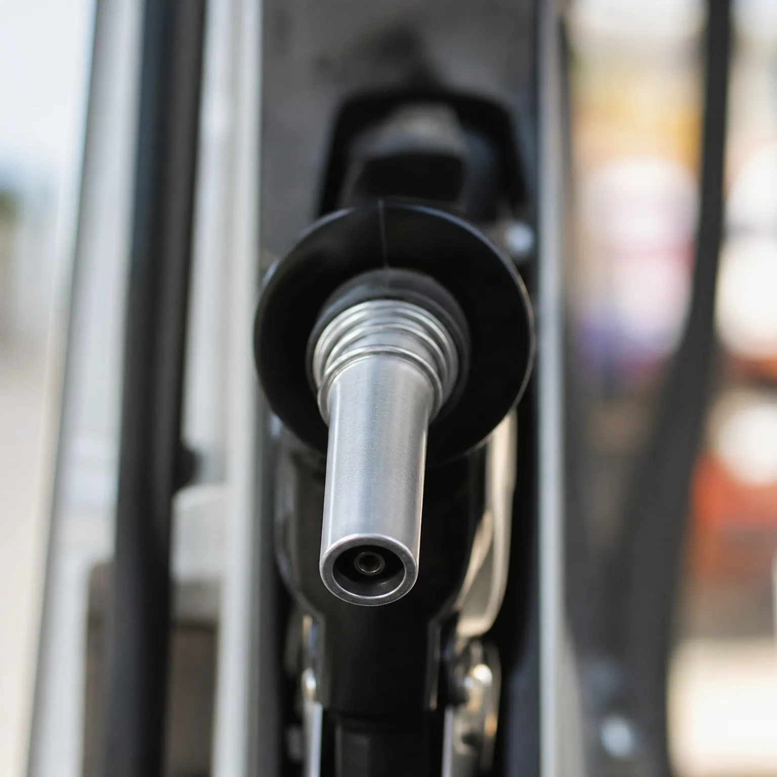Close-up of a black fuel nozzle with a metal spout mounted on a pump, with a blurred background.