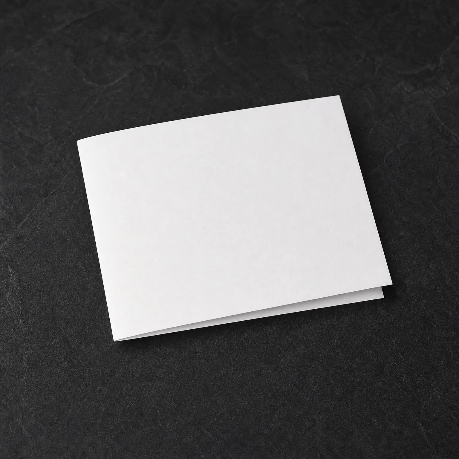 A blank white folded card lying closed on a dark gray textured surface.