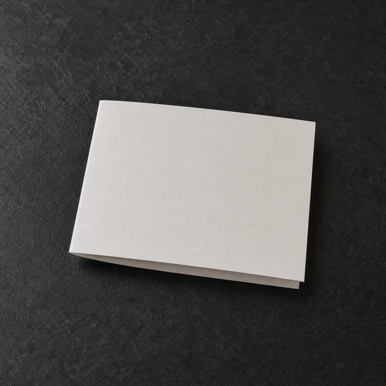 A blank folded white card lying on a dark textured gray surface.