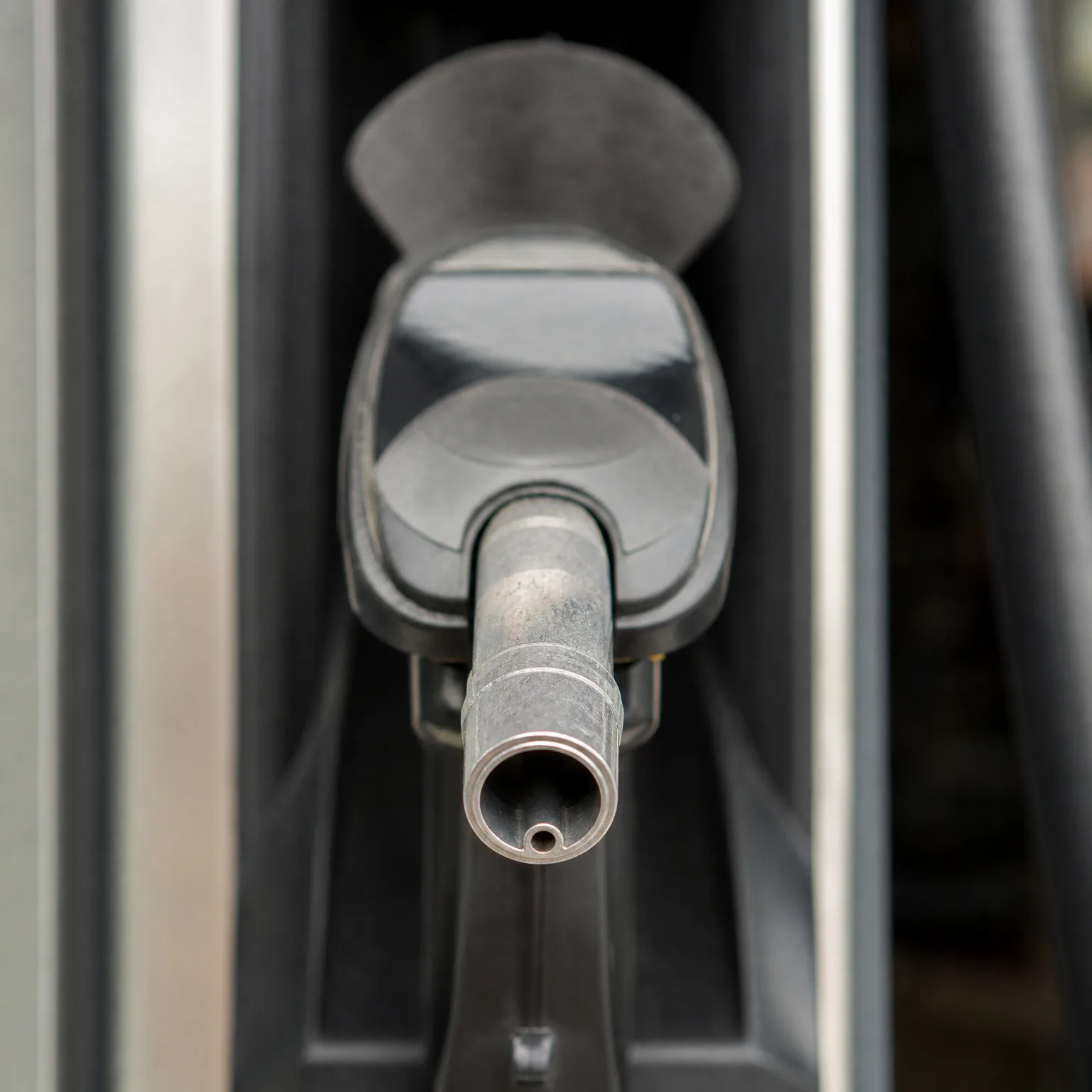 Close-up of a fuel nozzle with a metal spout pointing toward the camera, holstered in a gas pump.