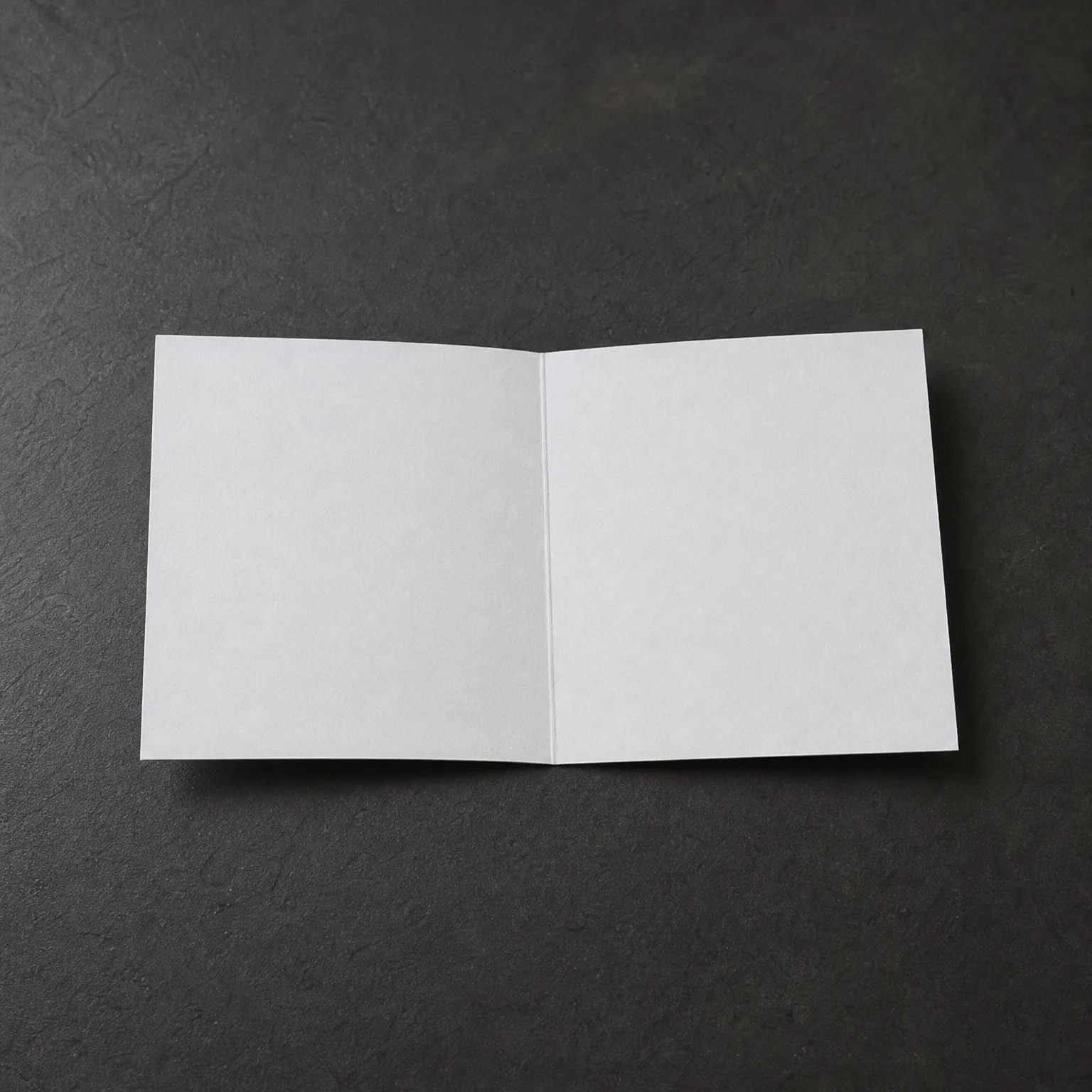 A blank white folded card standing open on a dark textured gray surface.