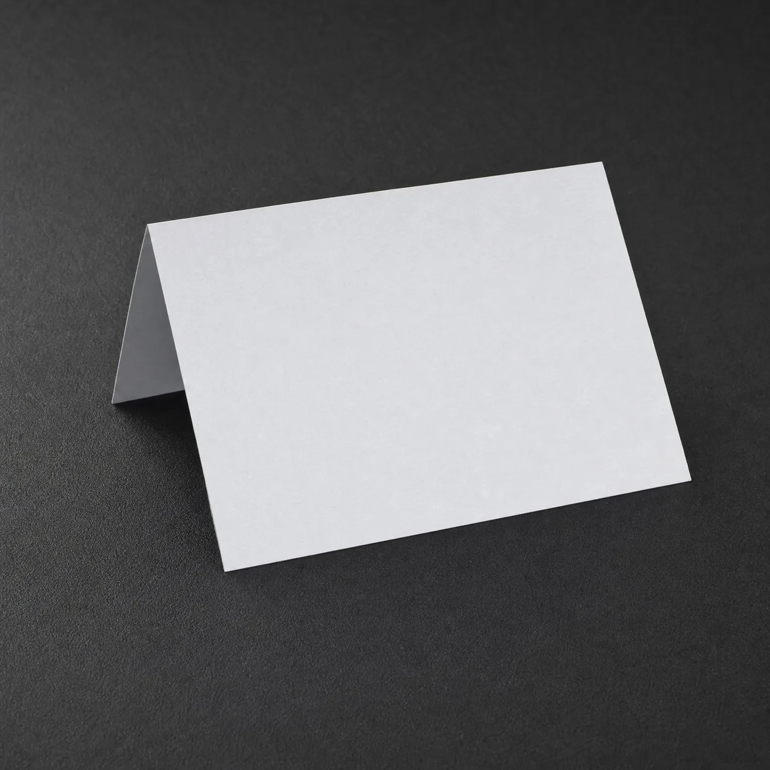 A blank white folded tent card standing on a dark gray textured surface.