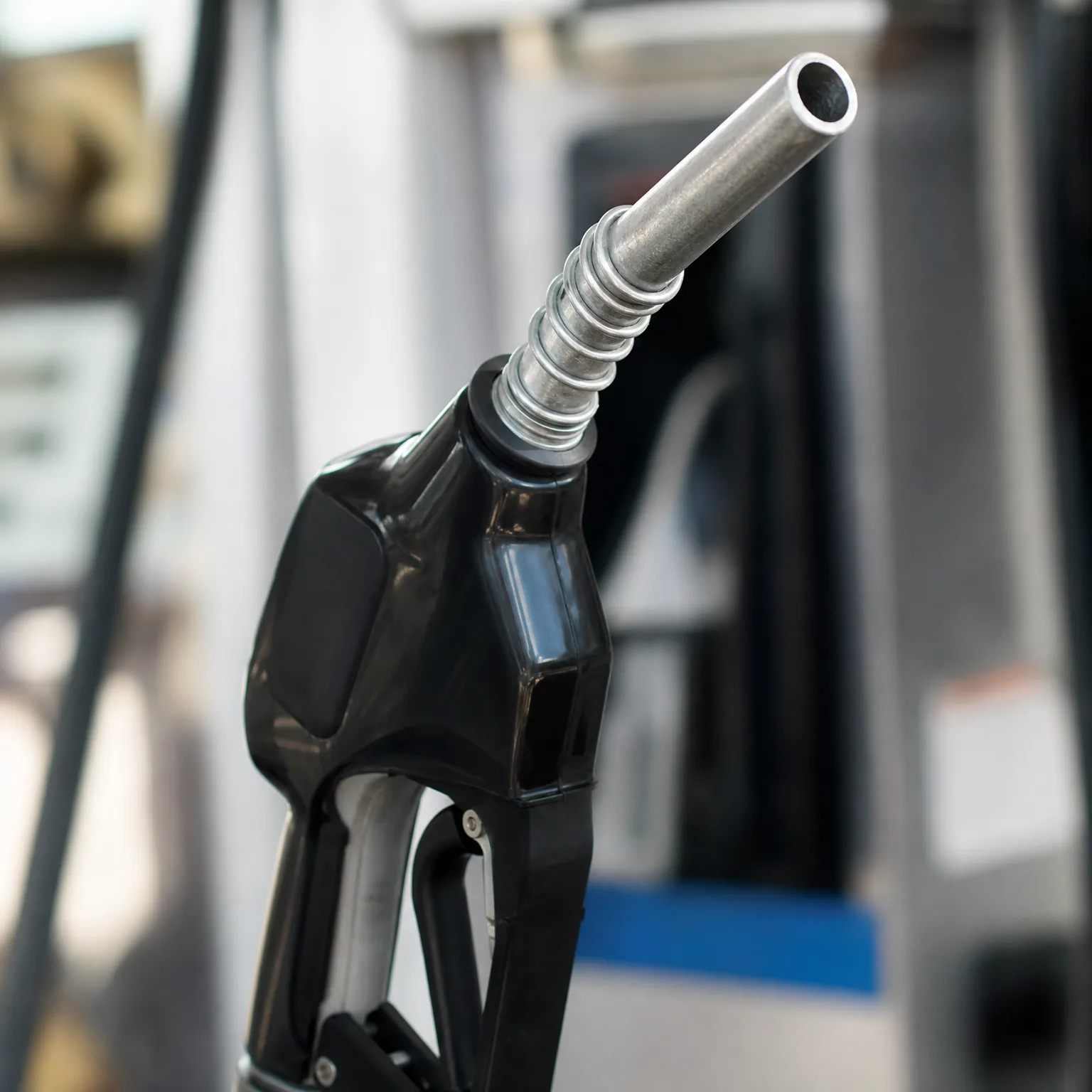 Close-up of a black fuel nozzle with a metal spout against a blurred background.
