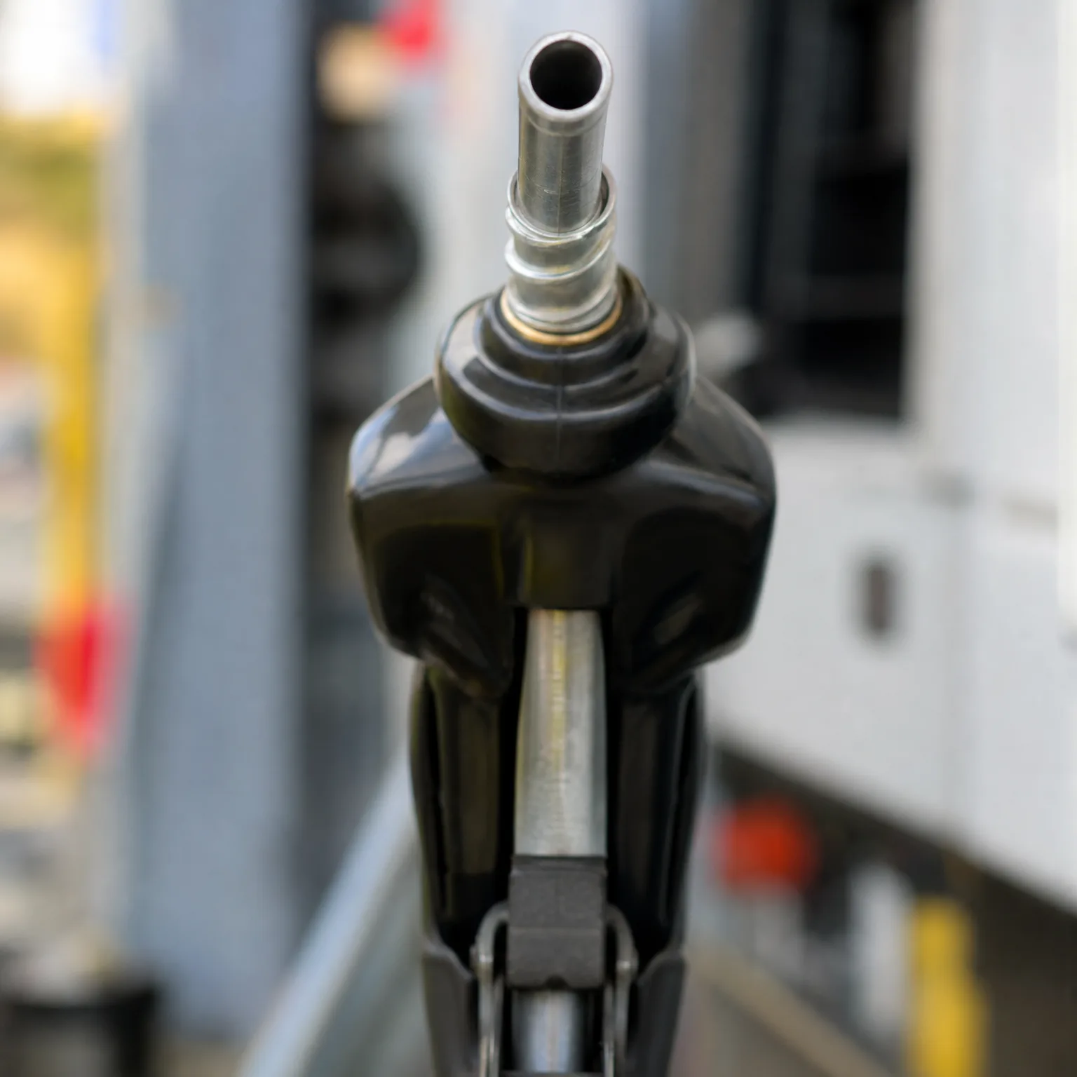 Close-up of a black fuel nozzle with a metal spout, photographed head-on against a blurred background.