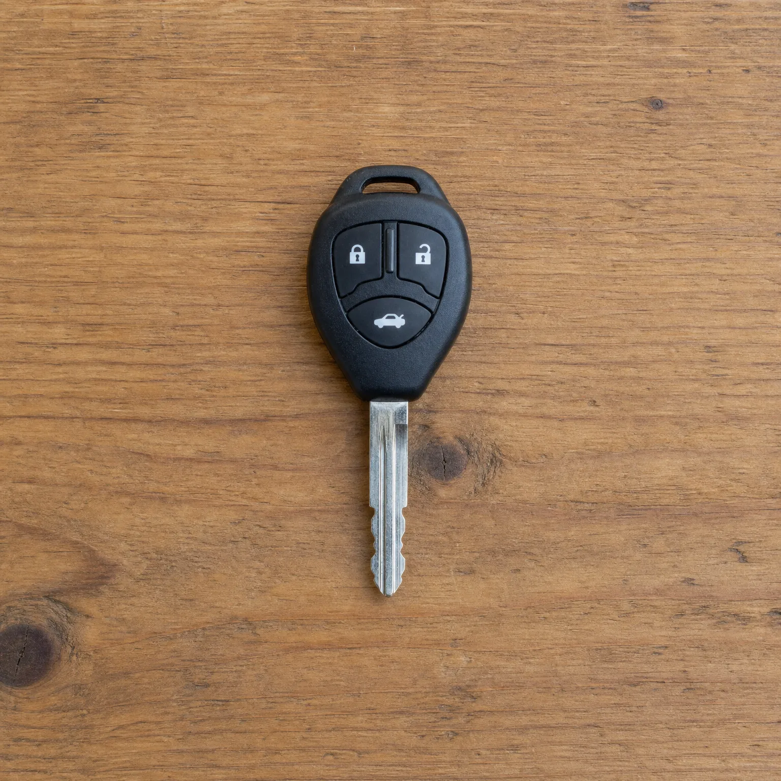 A black three-button remote car key with an uncut-style metal blade lying on a wooden surface.