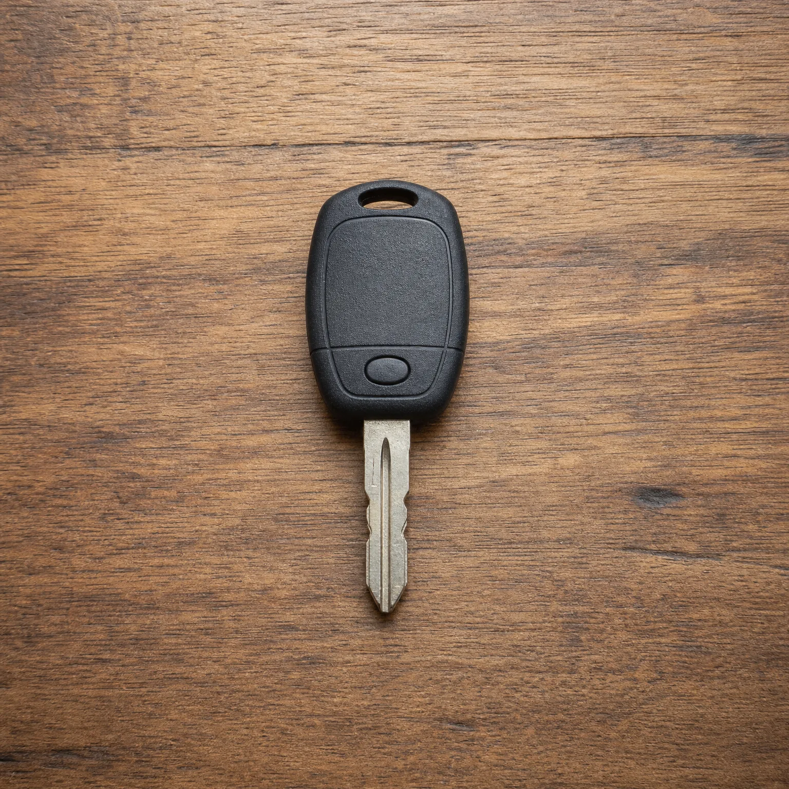A black plastic-headed car key with a single button and an uncut-looking metal blade lying on a brown wood surface.
