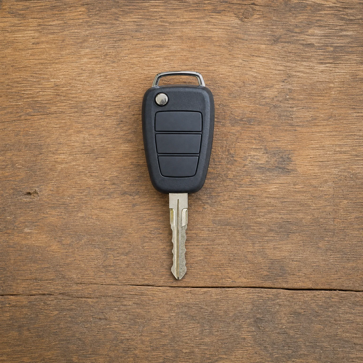 A black remote car key with three buttons and a metal blade lying on a weathered wooden surface.