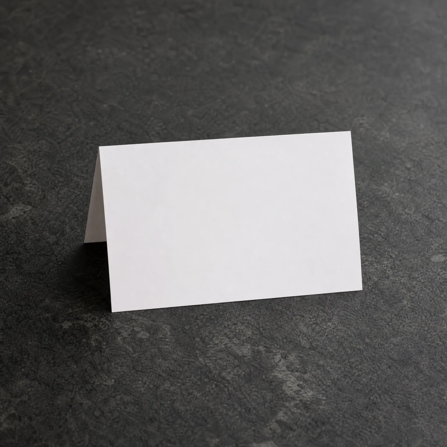 A blank white folded tent card standing on a dark gray textured stone surface.