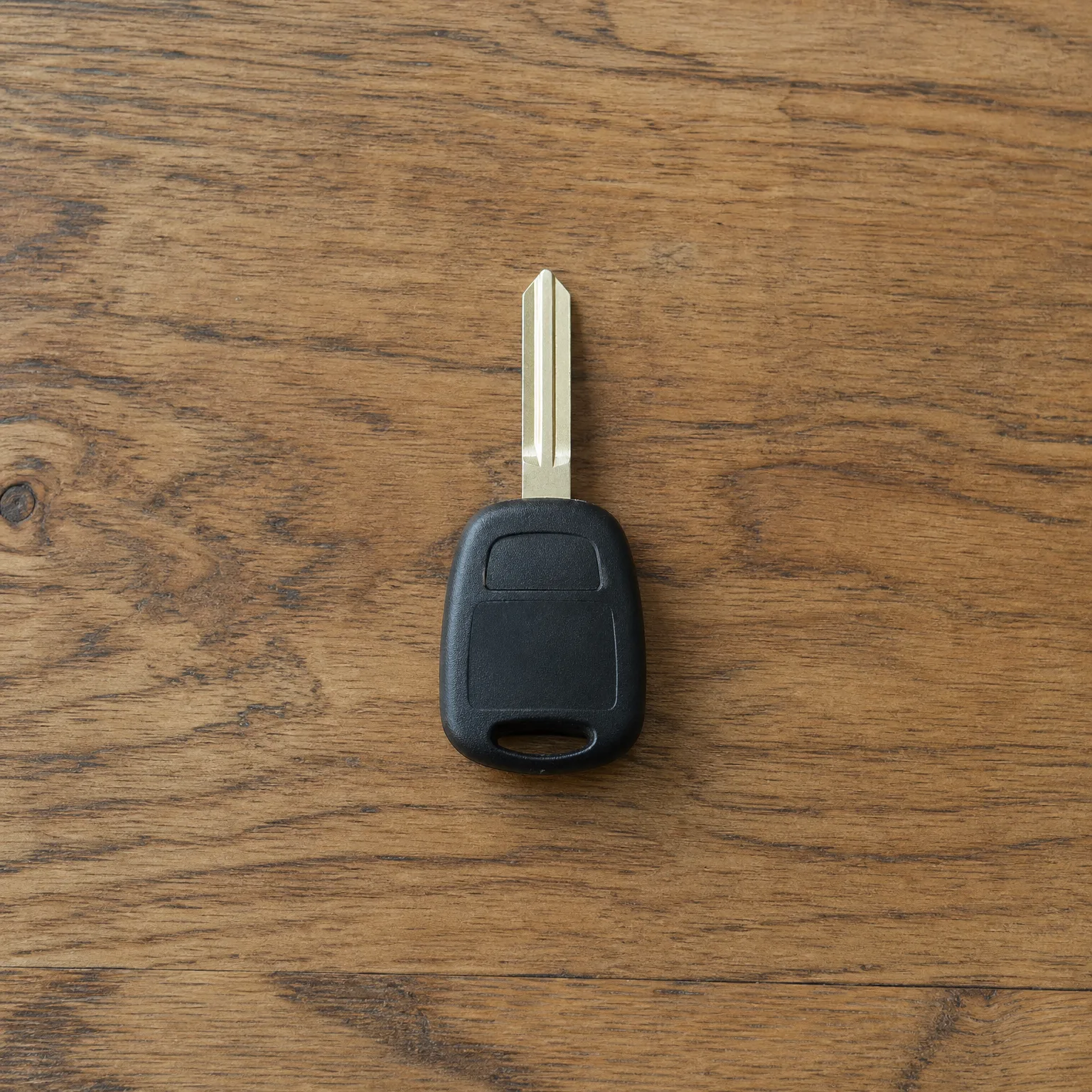 A car key with a black plastic head and uncut metal blade lying on a wooden surface.