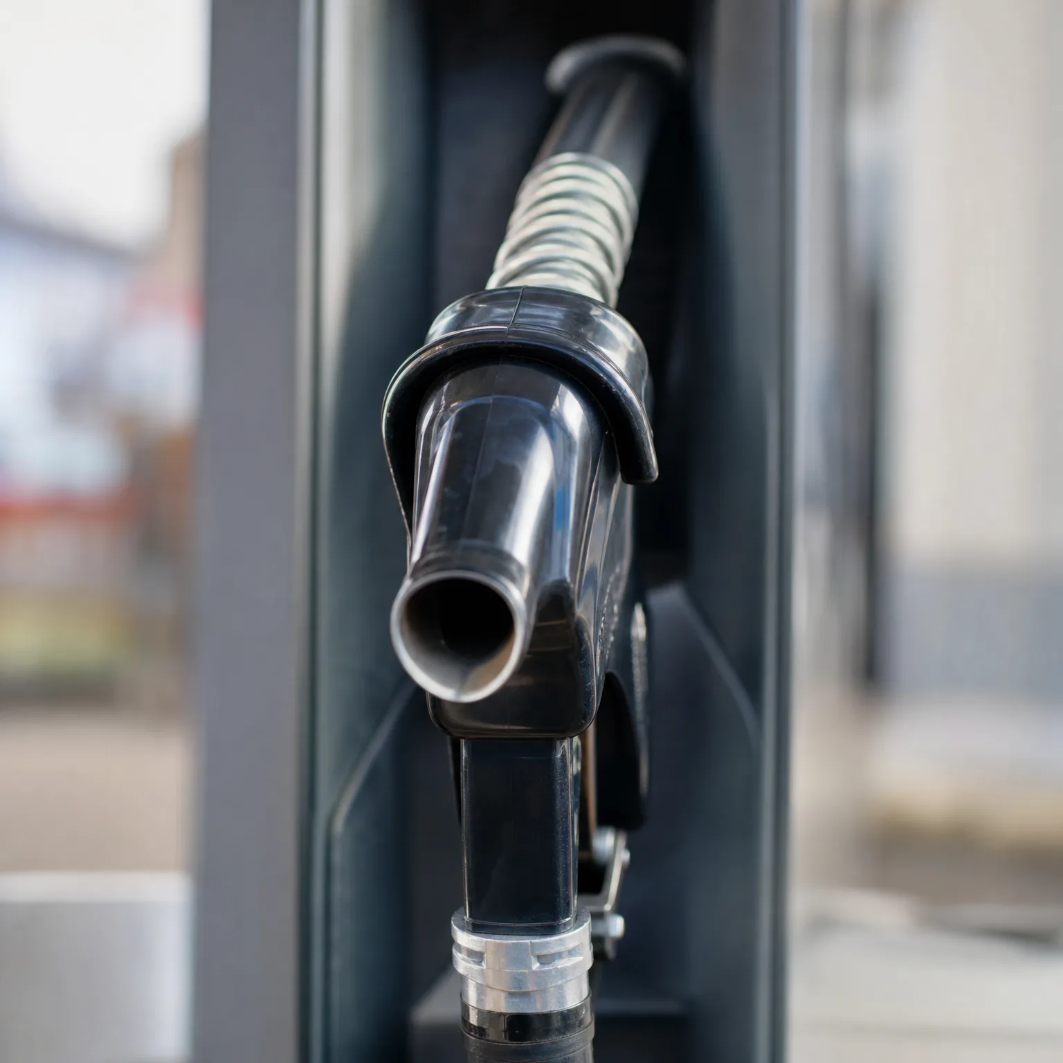 Close-up of a black fuel nozzle resting in a fuel dispenser, with a blurred background.