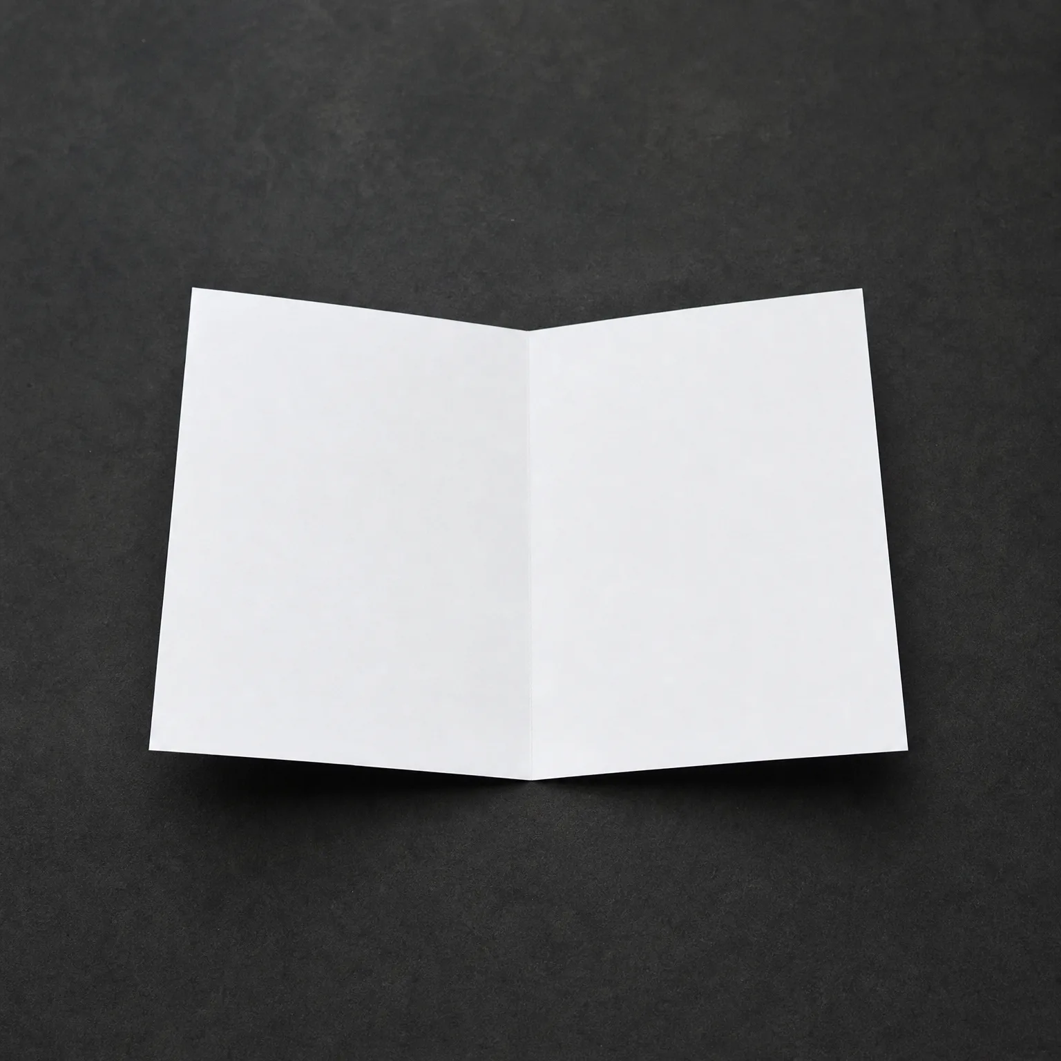A blank white folded card standing open in a V shape on a dark gray textured surface.