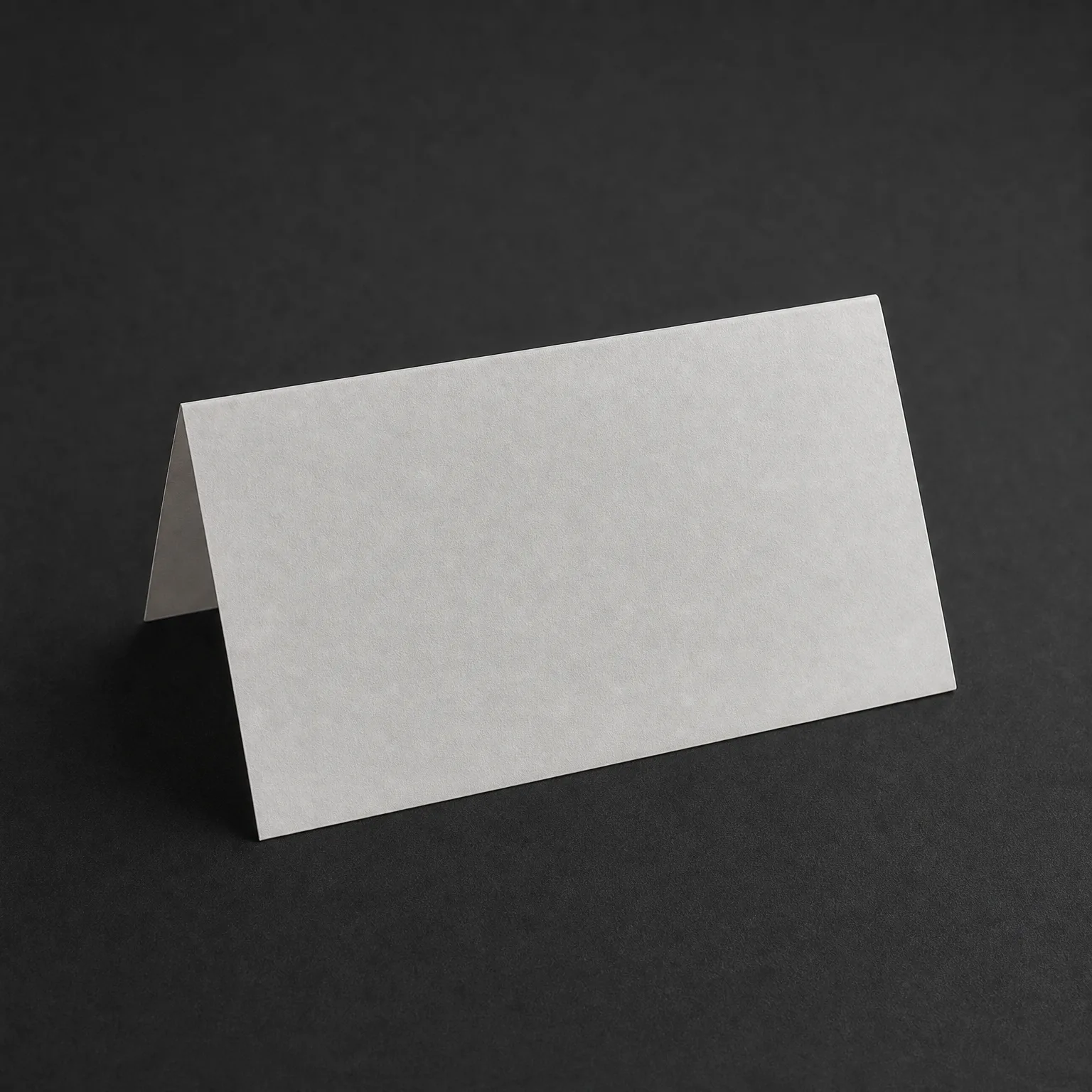 A blank white folded tent card standing upright on a dark gray textured surface.