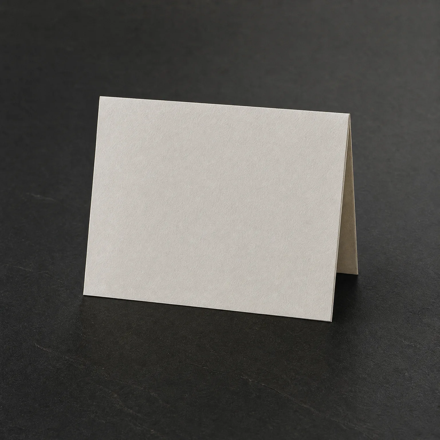 A blank folded white card standing tent-style on a dark gray textured surface.