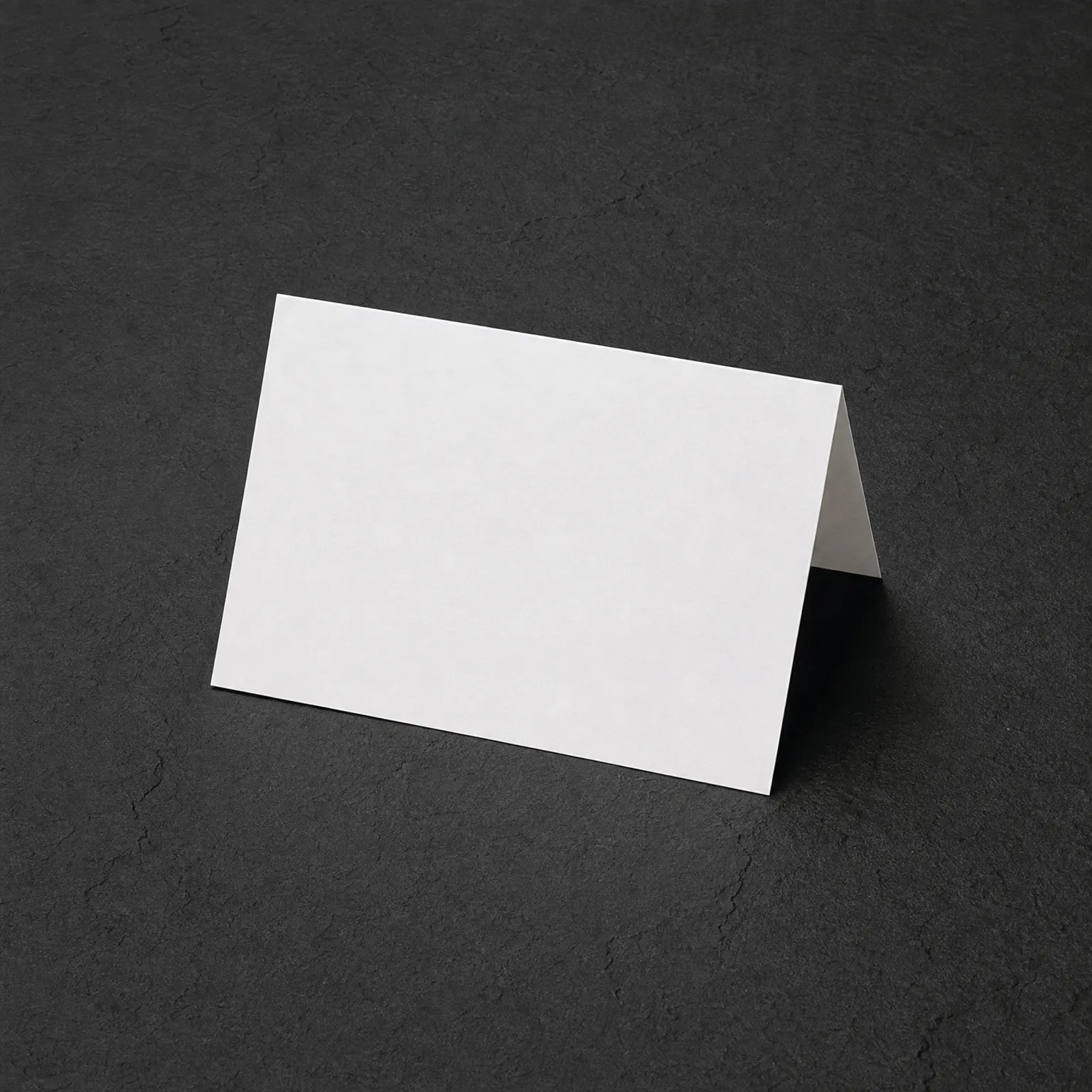 A blank white folded tent card standing on a dark textured gray surface.