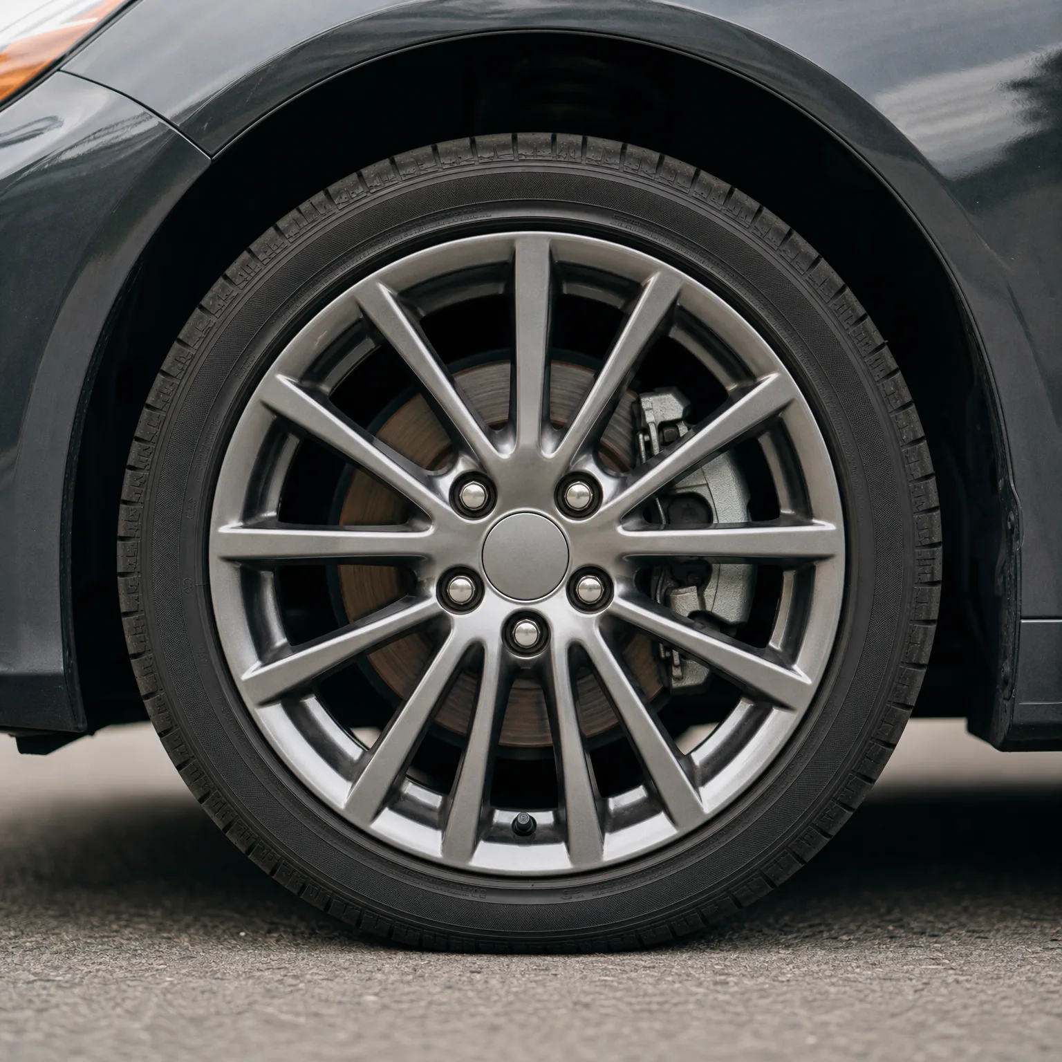 Close-up of a dark car's front wheel with a multi-spoke silver alloy rim and low-profile tire, parked on asphalt.