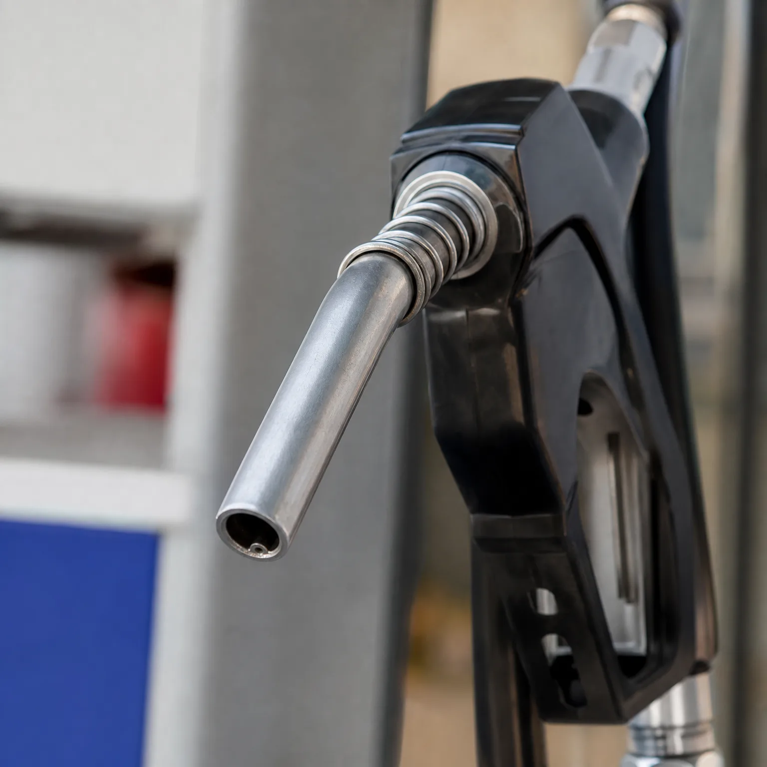 Close-up of a black fuel nozzle with a metal spout on a pump, against a blurred background.
