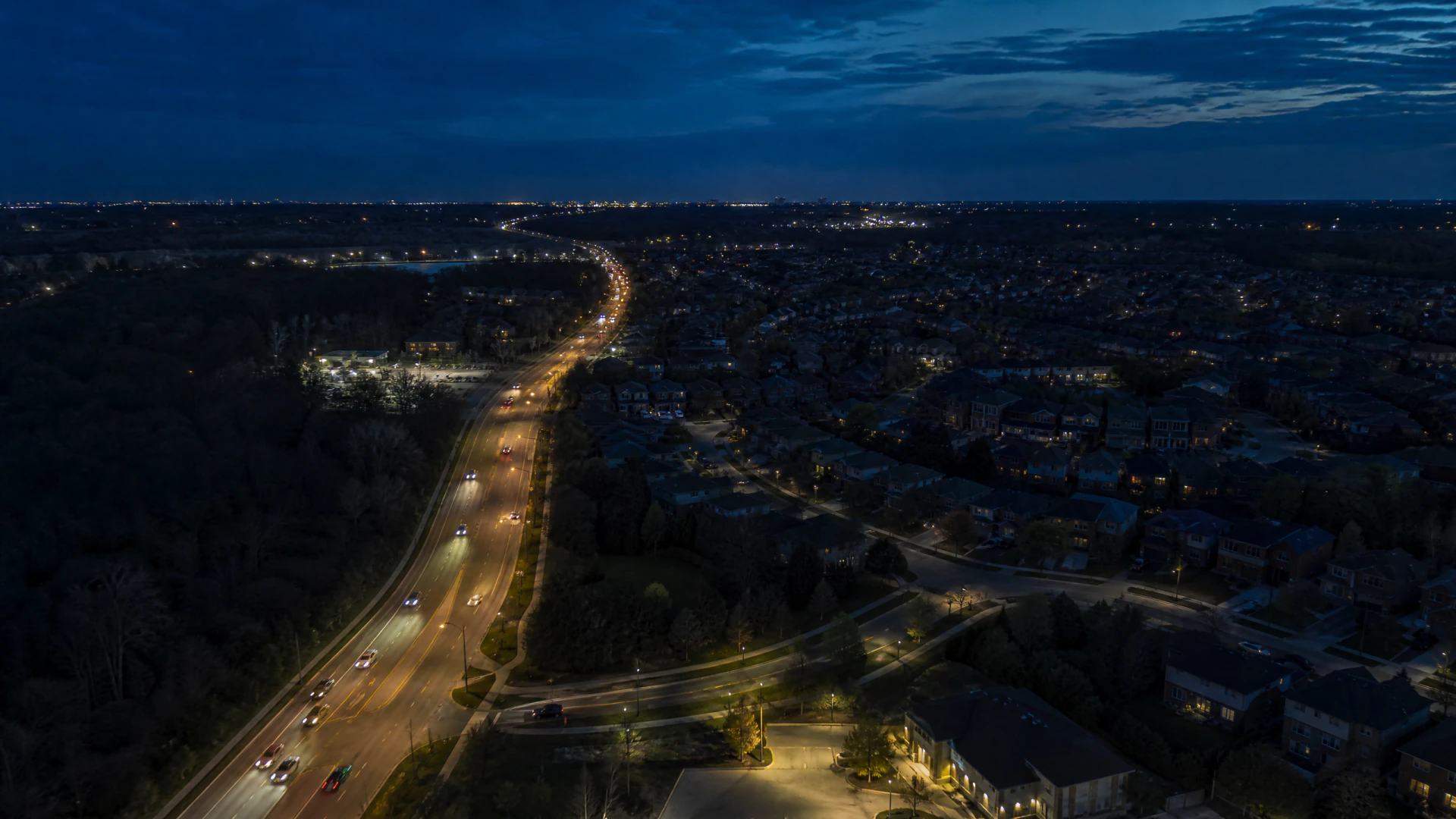 Aerial night view of a curved multi-lane road lined with street lights passing through a suburban residential neighborhood.