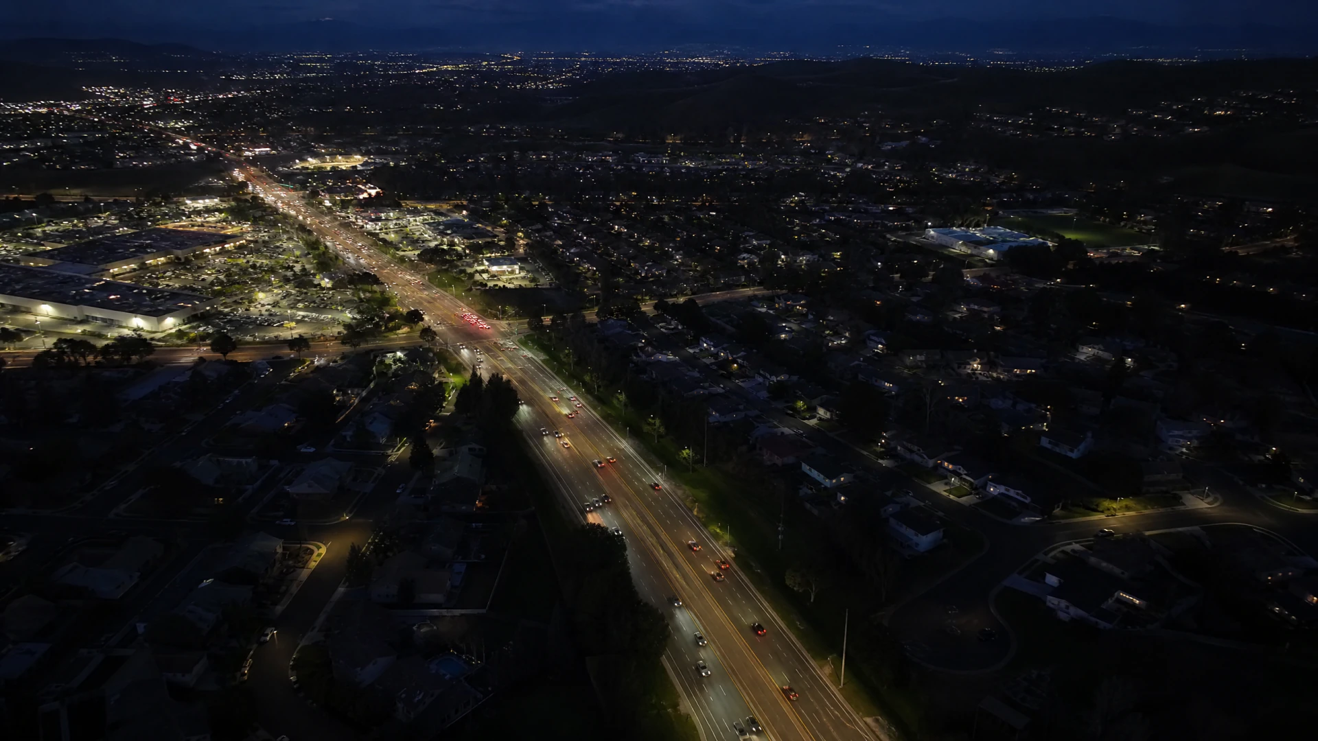 Aerial night view of a brightly lit multi-lane suburban boulevard flanked by residential and commercial development.
