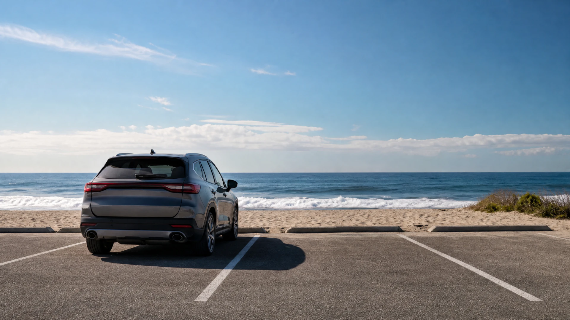 A dark gray SUV parked in a beachfront lot, facing the ocean and sandy shore.