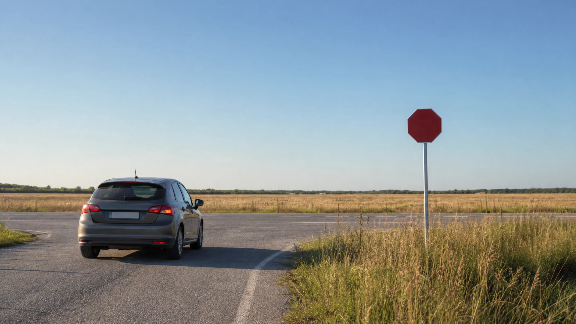 A silver hatchback pauses at a rural road junction next to a blank red stop sign.