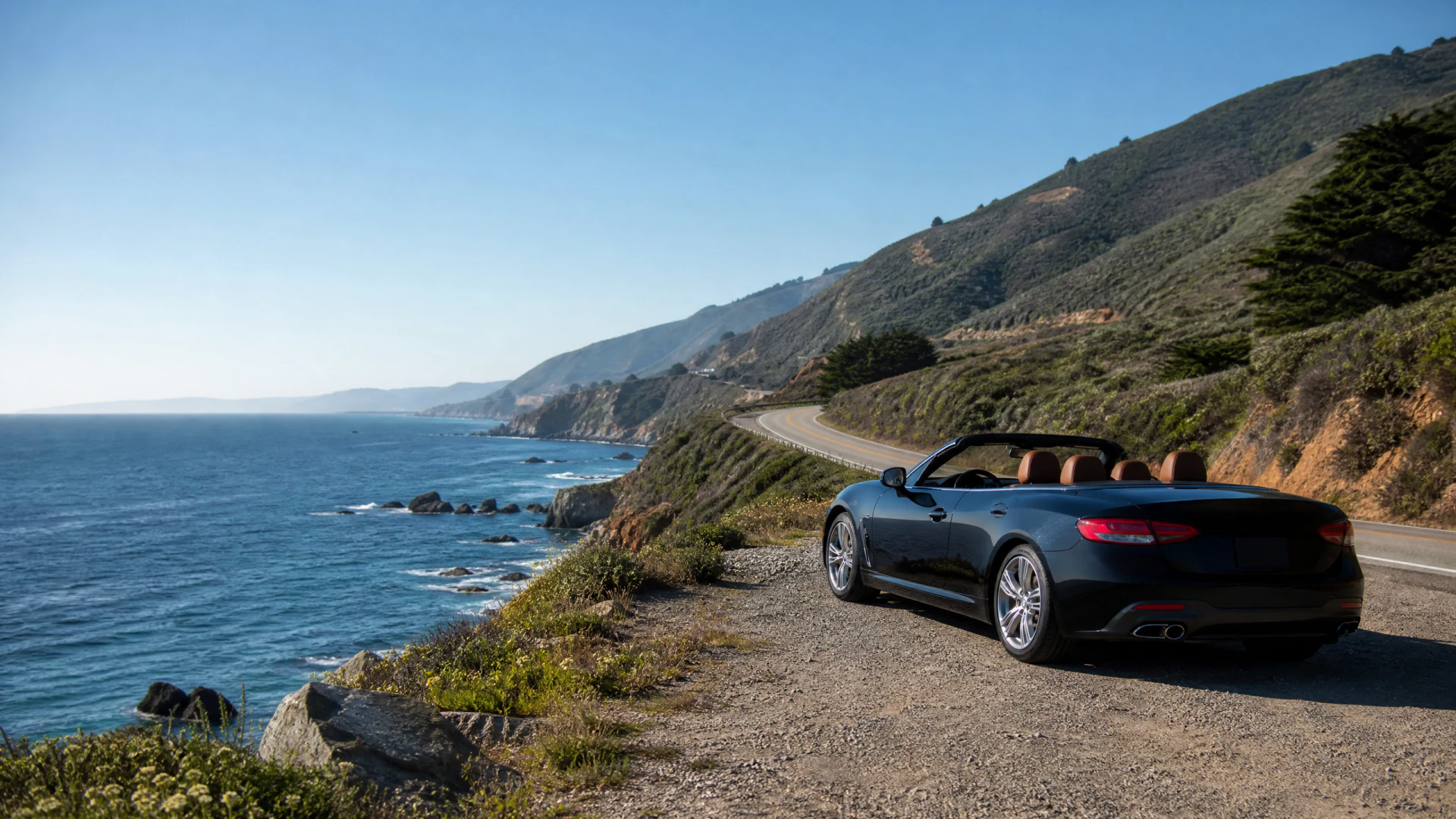 A black open-top convertible parked on a narrow gravel shoulder of a cliffside coastal road overlooking the ocean.