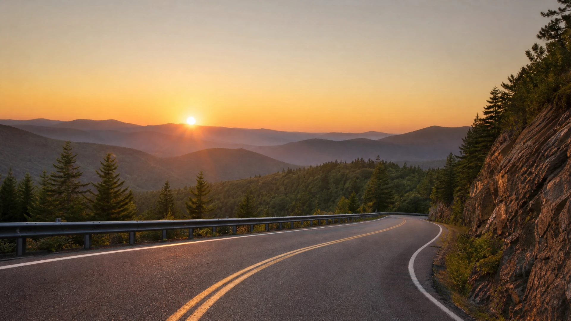 A winding two-lane road curves along a rocky mountain cliff at sunset, with layered forested ridges visible in the background.