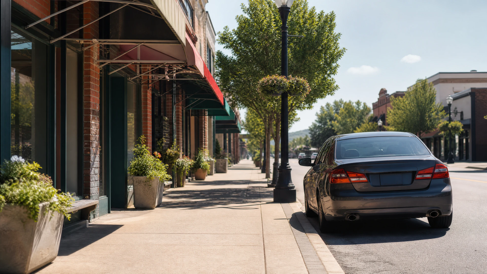 A dark gray sedan parked on a sunny small-town main street beside brick storefronts with colorful awnings and tree-lined sidewalks.
