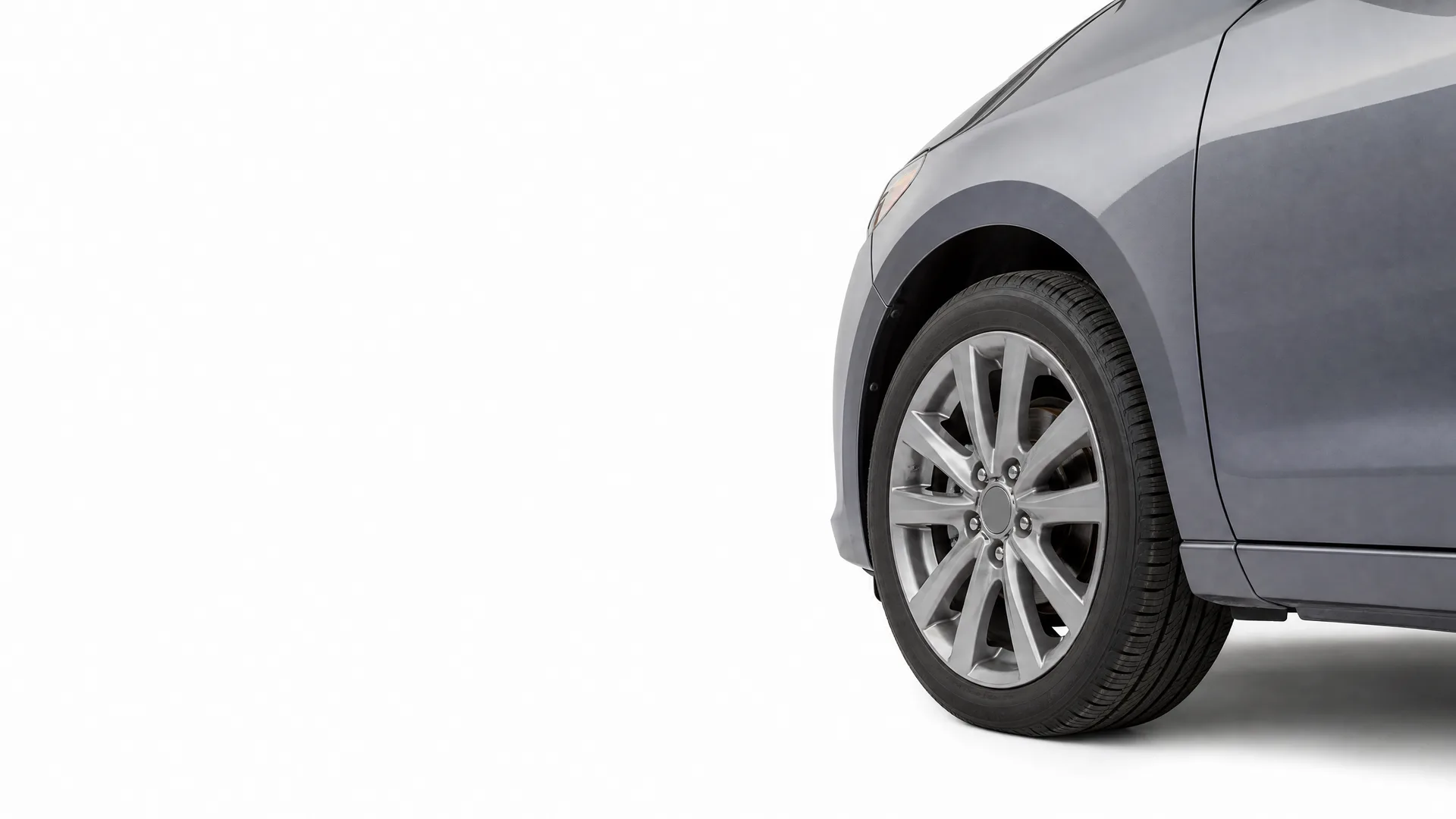 Front corner of a gray car, showing the front wheel with a multi-spoke alloy wheel, tire and lower fender, against a plain white background.