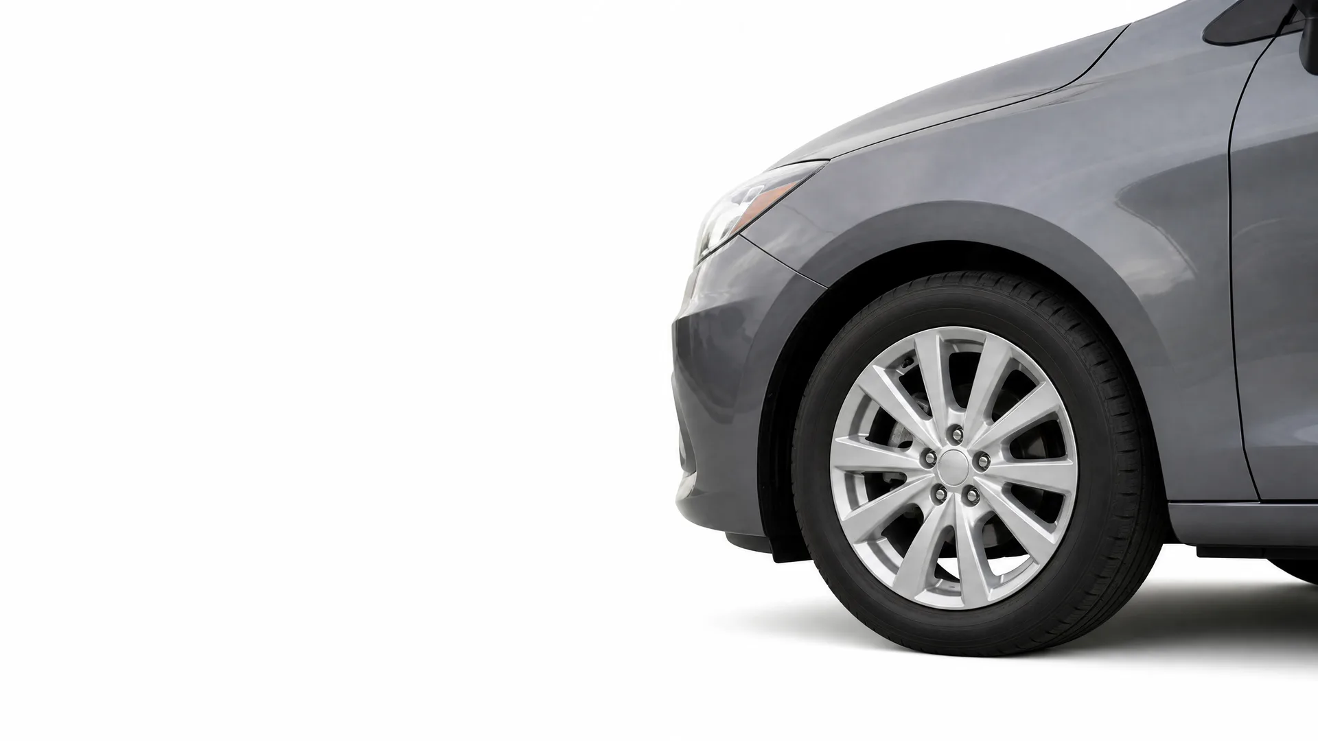 Front portion of a gray car, showing the front wheel with a multi-spoke alloy wheel, fender and headlight edge, against a plain white background.