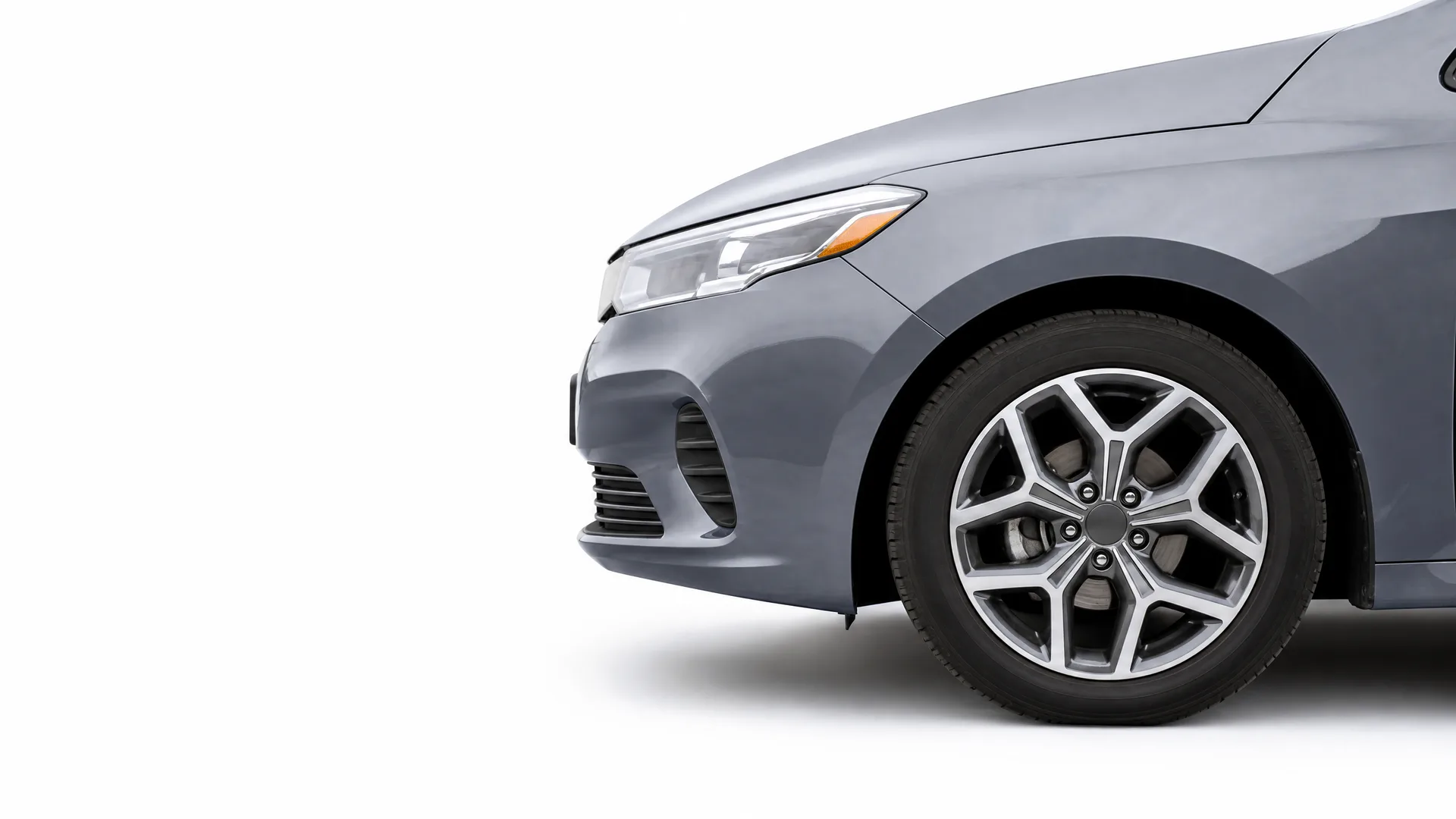 Front section of a gray sedan, showing the headlight, bumper, fender and alloy front wheel, against a plain white background.