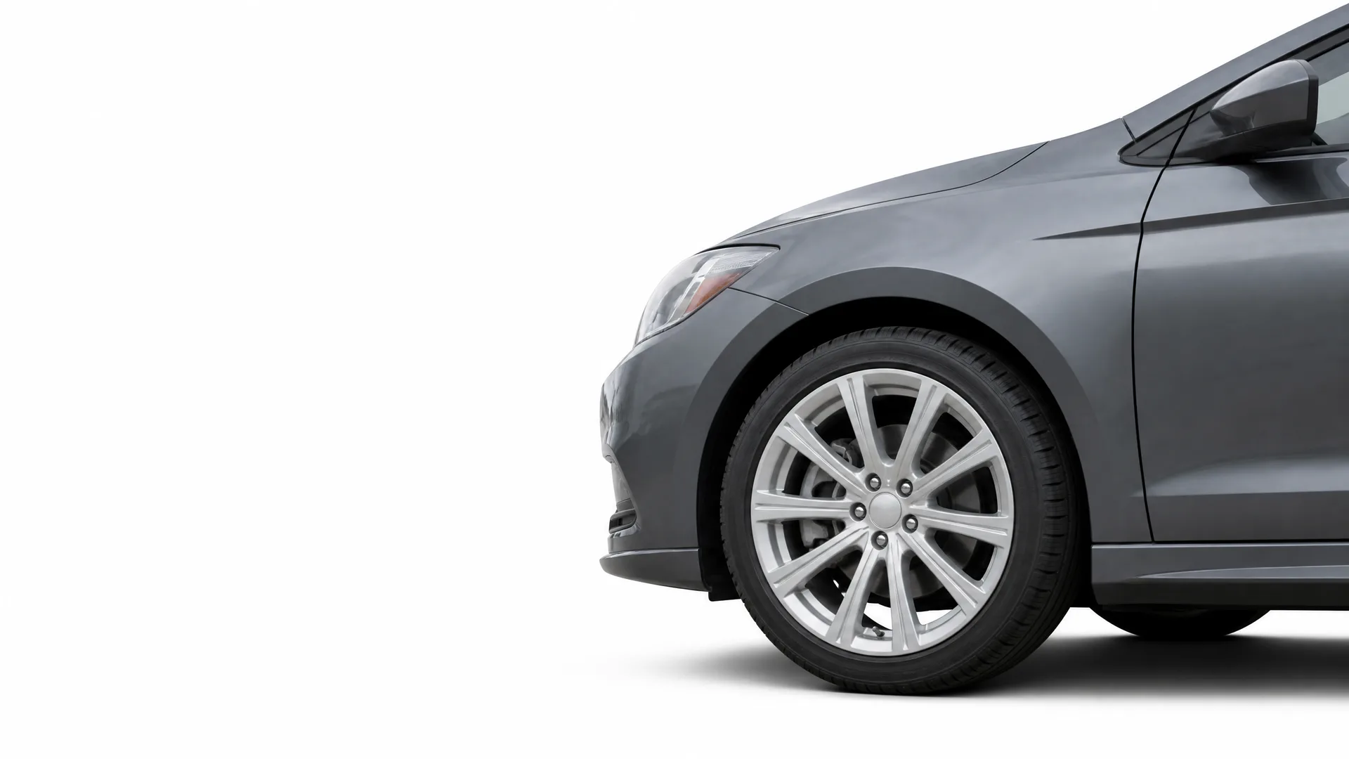 Front portion of a dark gray sedan, showing the front wheel with a multi-spoke alloy rim, fender, headlight edge and side mirror, against a plain white background.