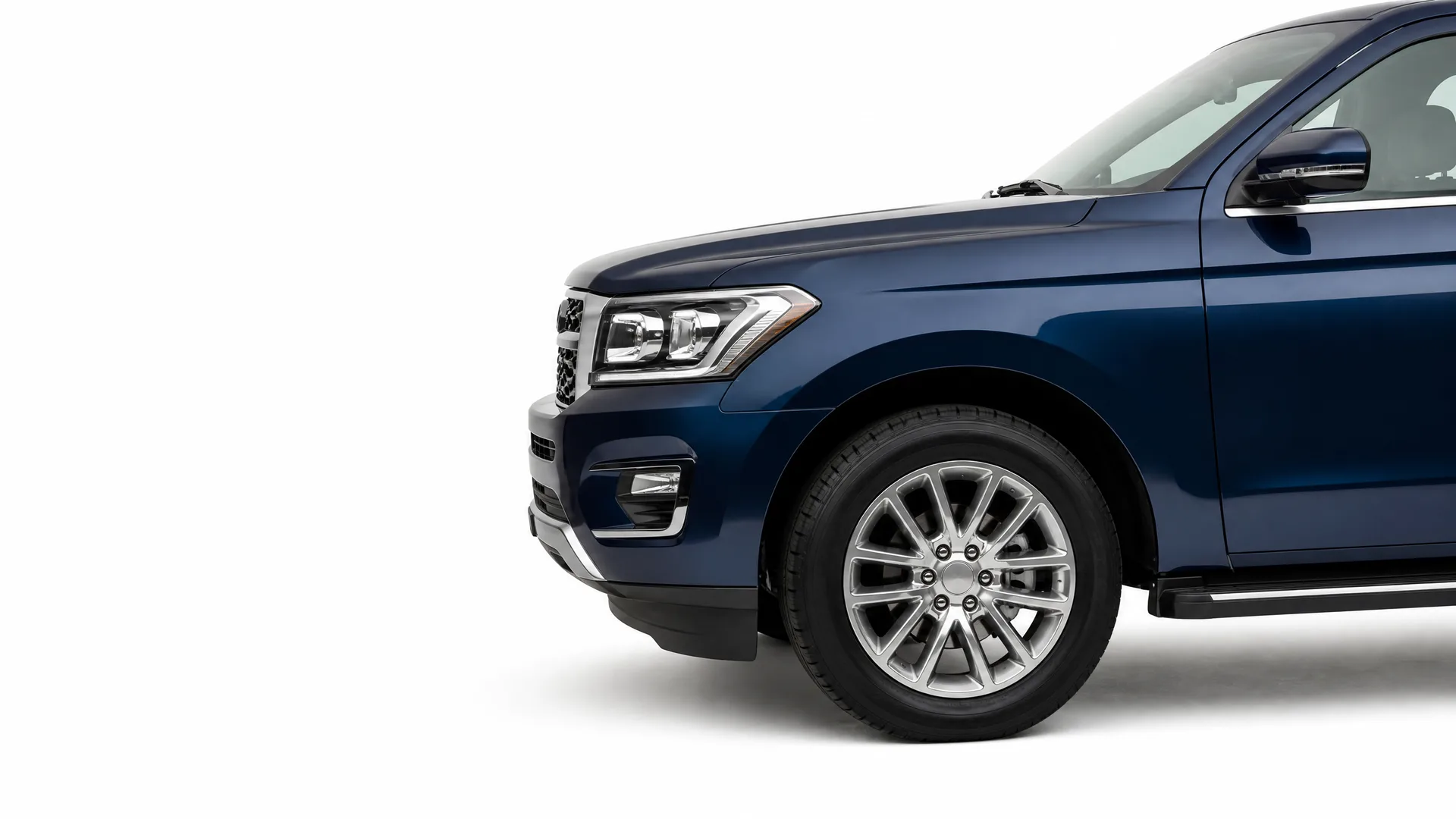 Front half of a dark blue full-size SUV photographed in profile against a plain white background, showing the headlight, front wheel with multi-spoke alloy rim, side mirror and running board.