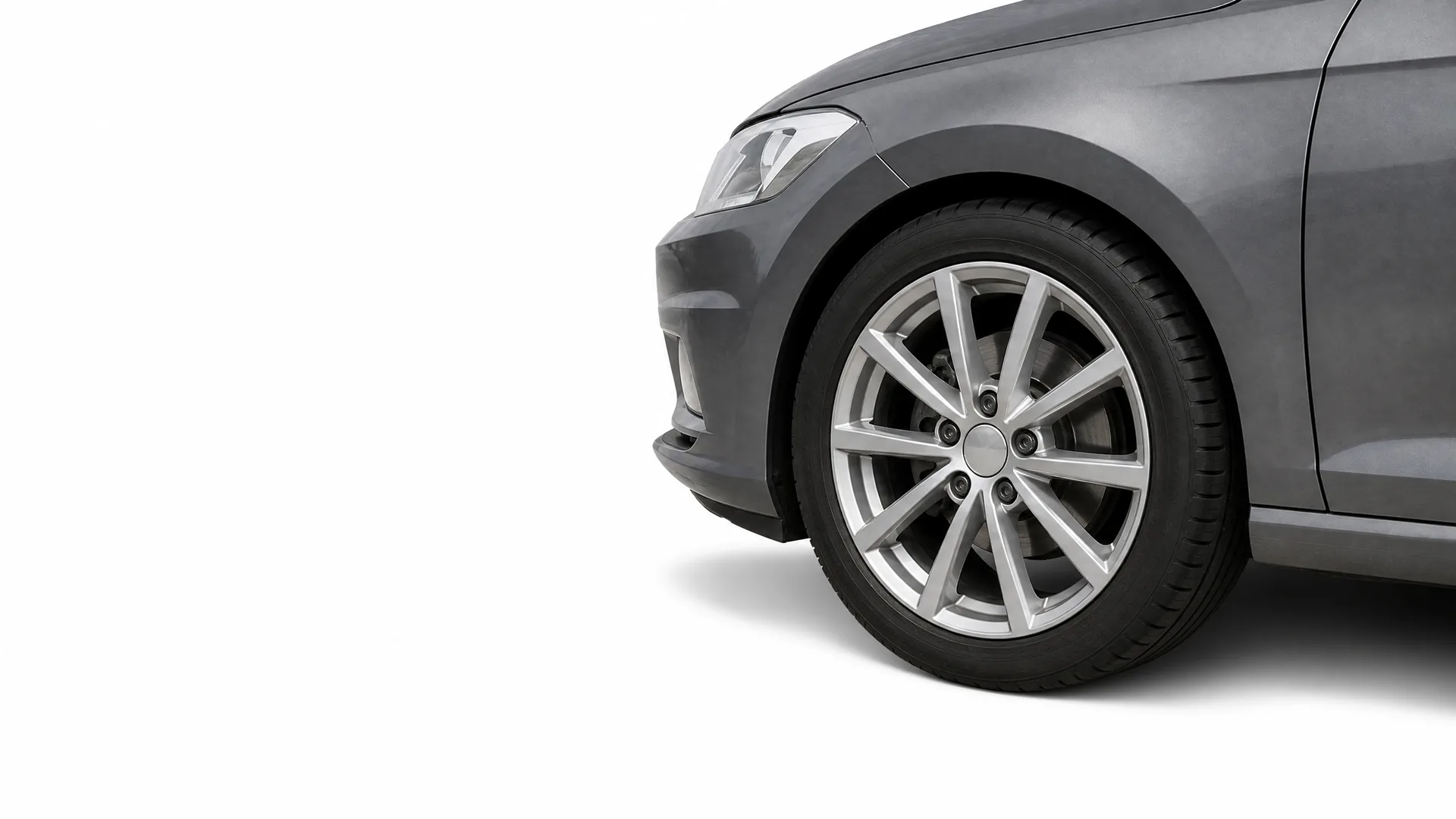 Front section of a dark gray car, showing the front wheel with a multi-spoke alloy rim, bumper and headlight, against a white background.