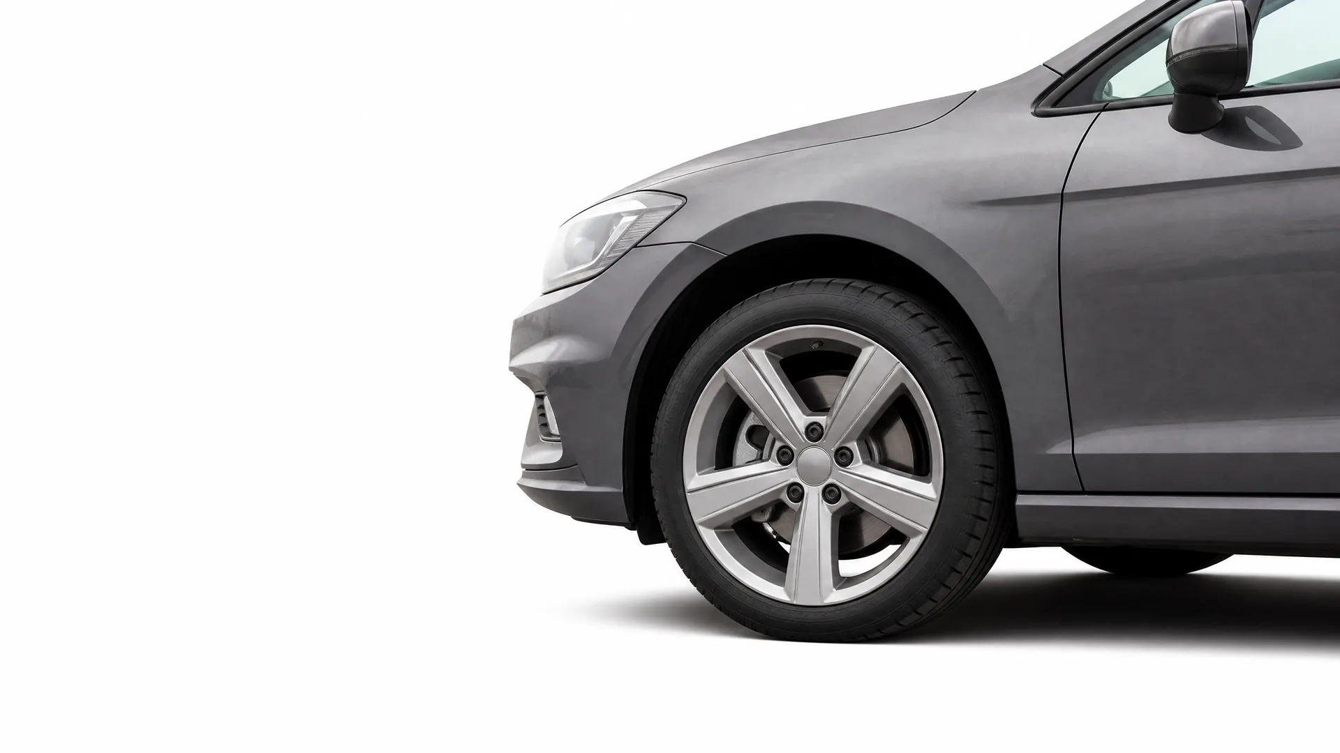 Front section of a dark grey car, showing the front wheel with a five-spoke alloy wheel, headlight, bumper and side mirror, against a white background.